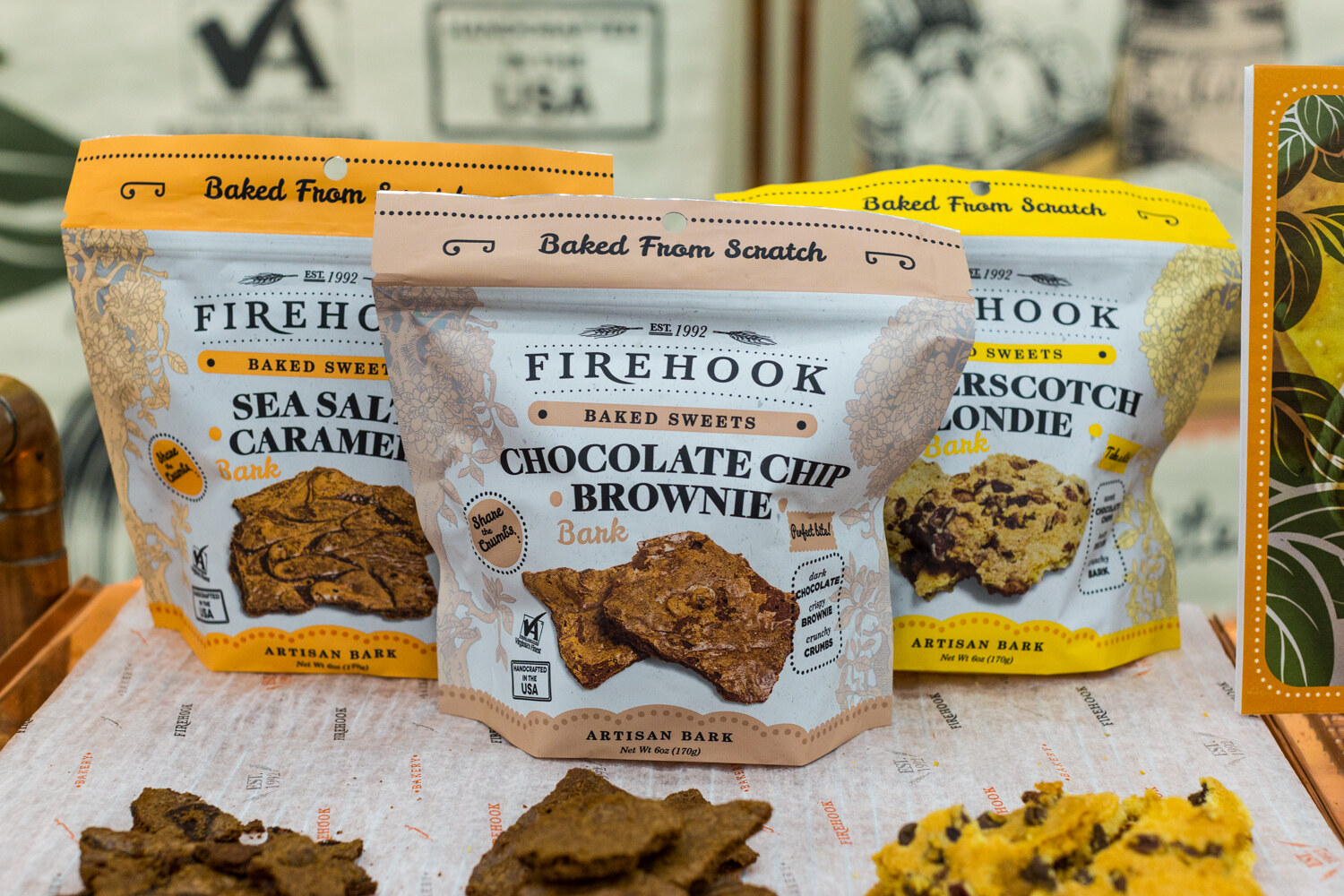 Three Firehook Baked Sweets Artisan Bark pouches on white paper with pieces of bark in front.