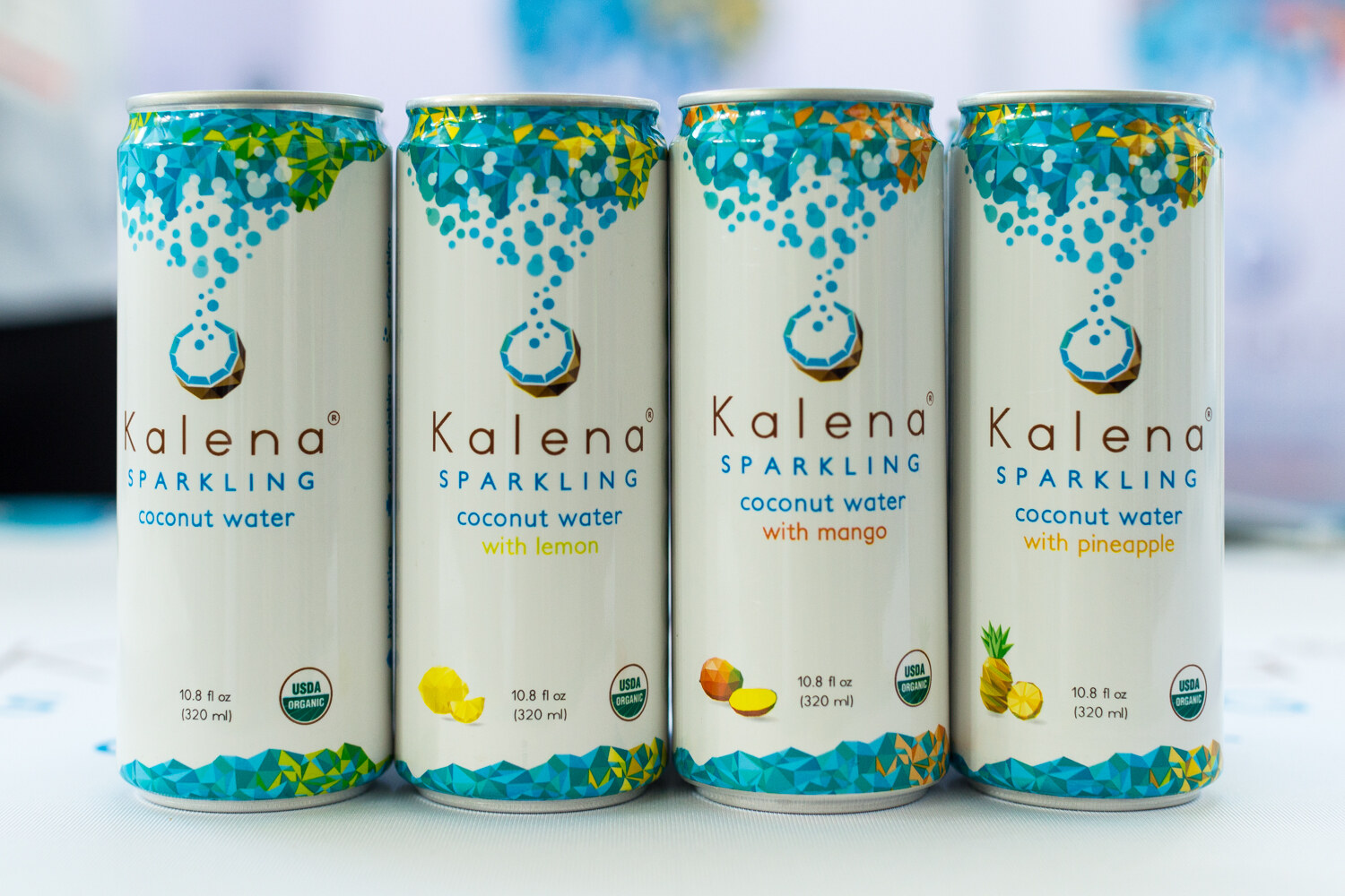Four white Kalena Sparkling coconut water cans with teal geometric tops on a white table.