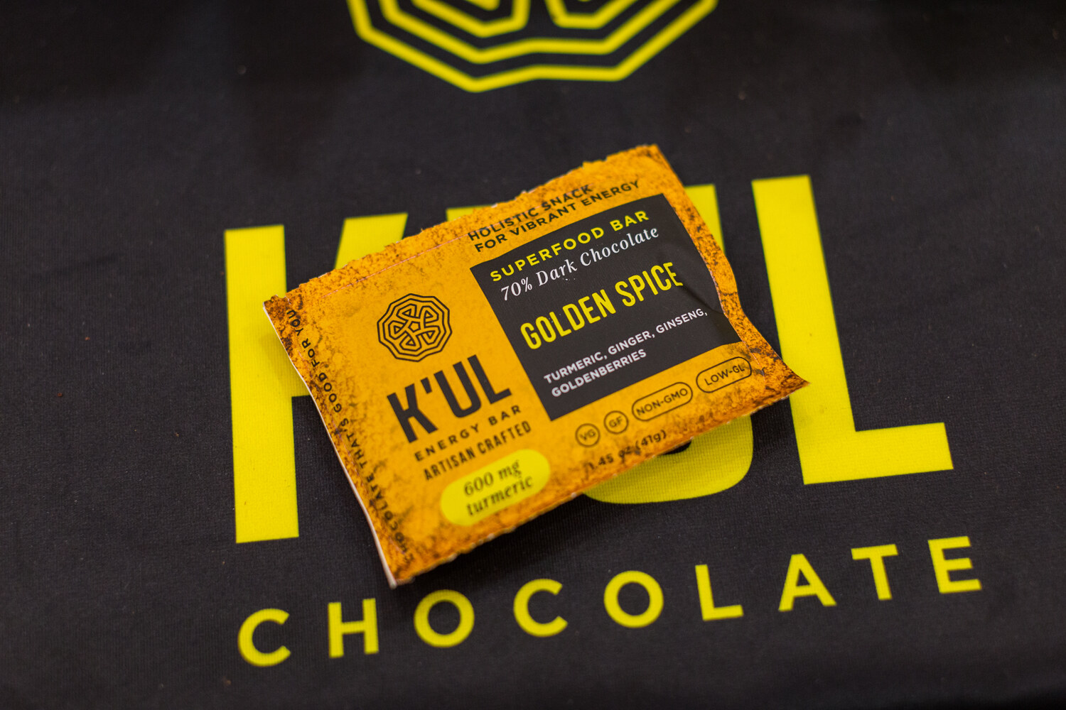 A yellow K'UL Golden Spice superfood bar wrapper on a black tablecloth with large yellow K'UL Chocolate lettering.