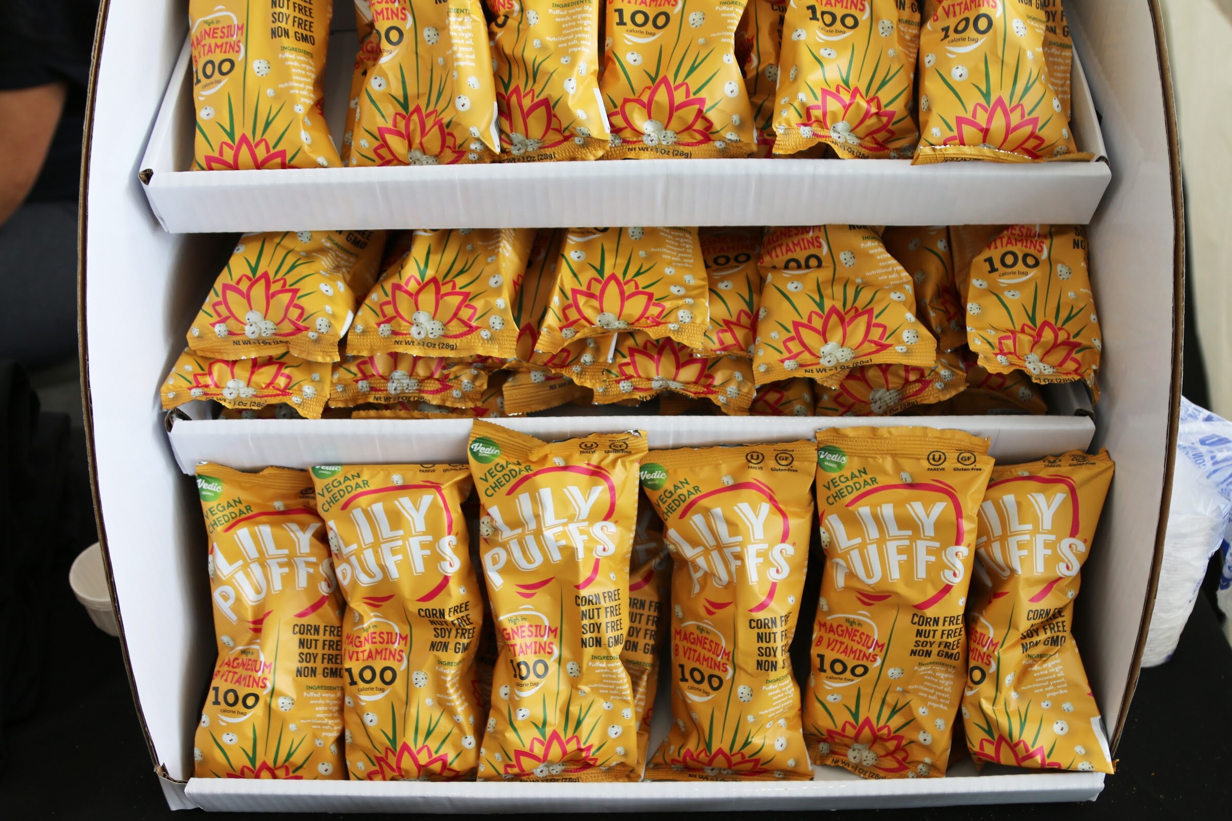 Rows of yellow Lily Puffs bags with a pink lotus design stacked on white cardboard display shelves.