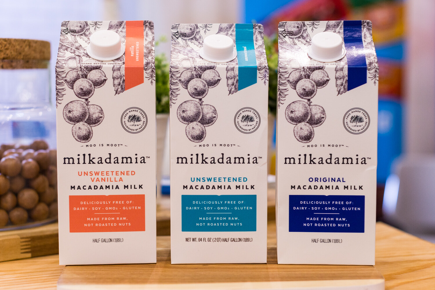 Three half-gallon Milkadamia cartons with macadamia illustrations and orange, teal and navy labels.