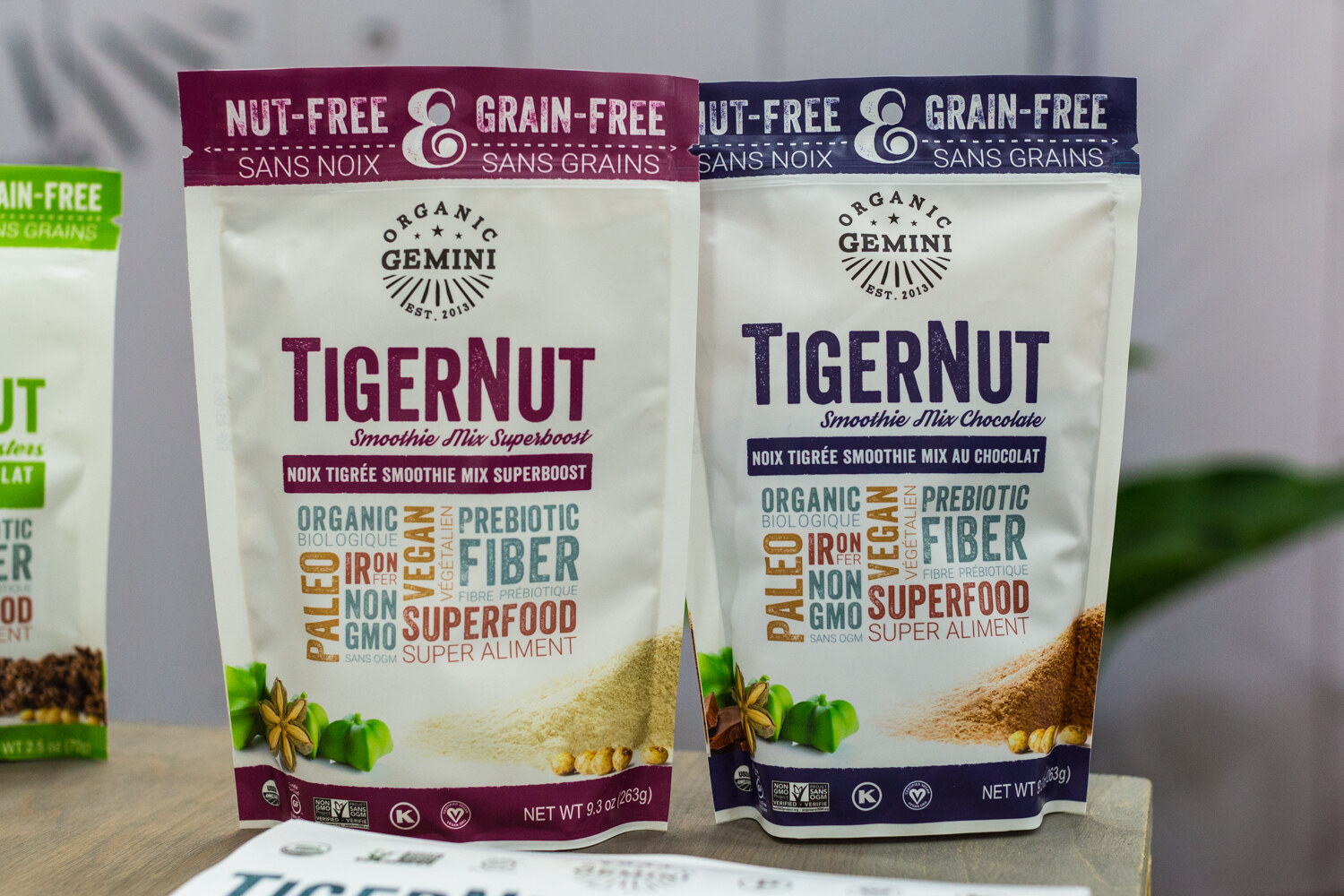 Two white pouches with plum and navy bands labeled TigerNut Smoothie Mix, Organic Gemini, standing on a wooden table.