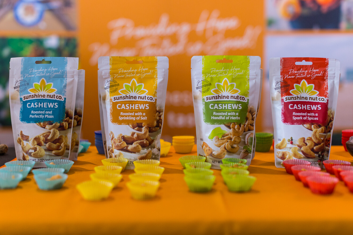 Four Sunshine Nut Co. cashew pouches in blue, yellow, green and red, with rows of small silicone cups in the same colors.