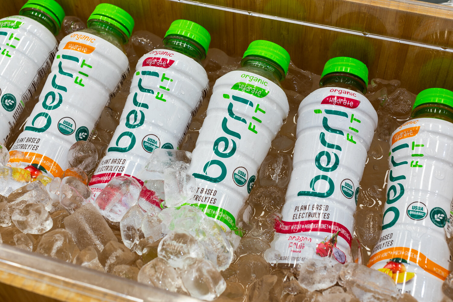 White Berri Fit bottles with green caps resting in ice in a wooden bin.
