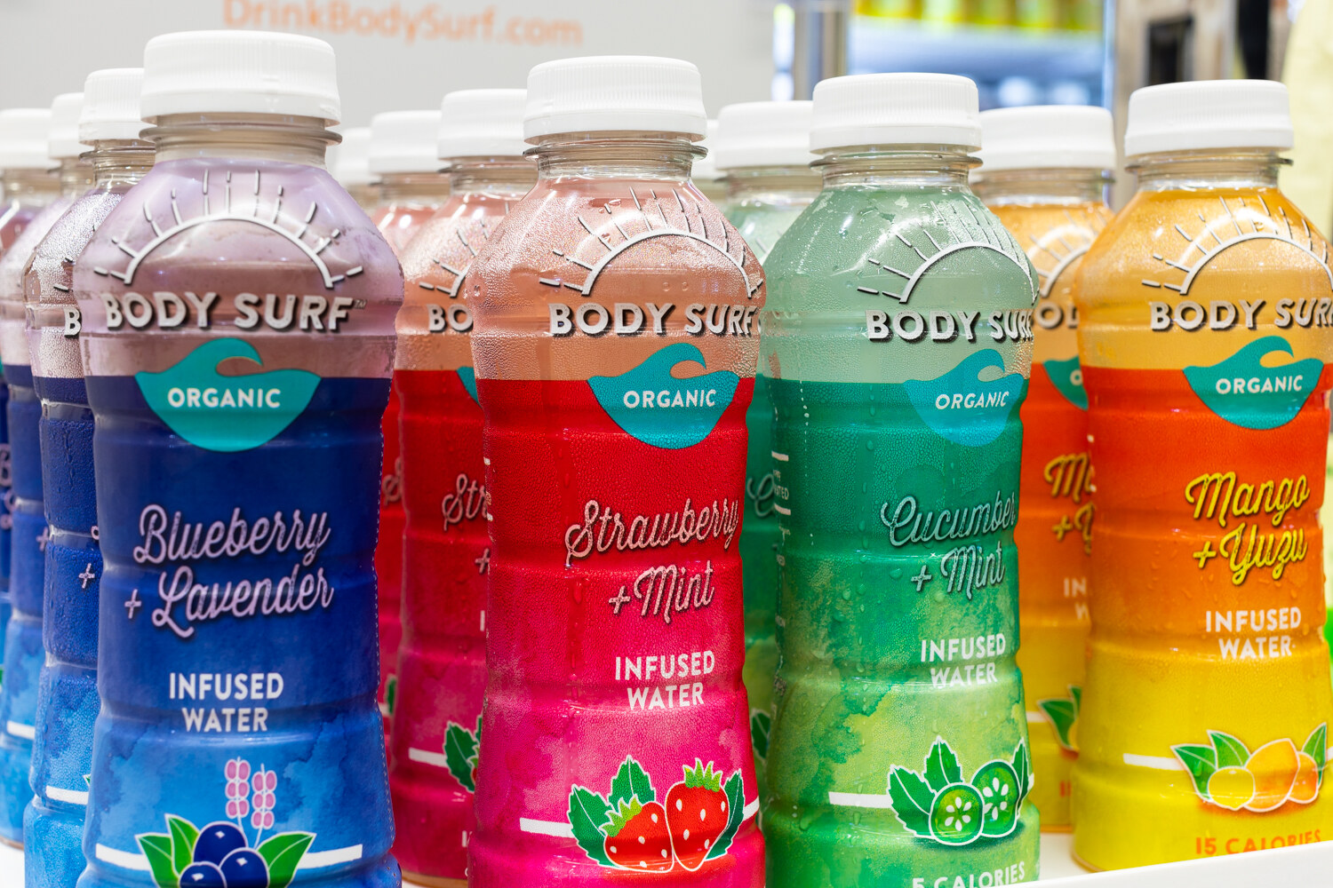A row of Body Surf bottles in blue, red, green and orange with watercolor-style labels.