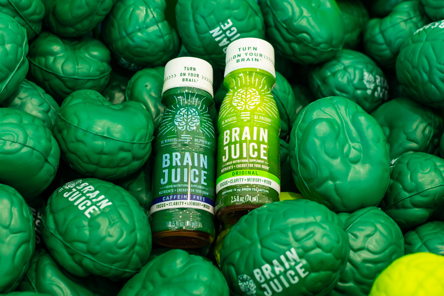Two small Brain Juice bottles lying among green squeezable brain toys printed with the Brain Juice name.