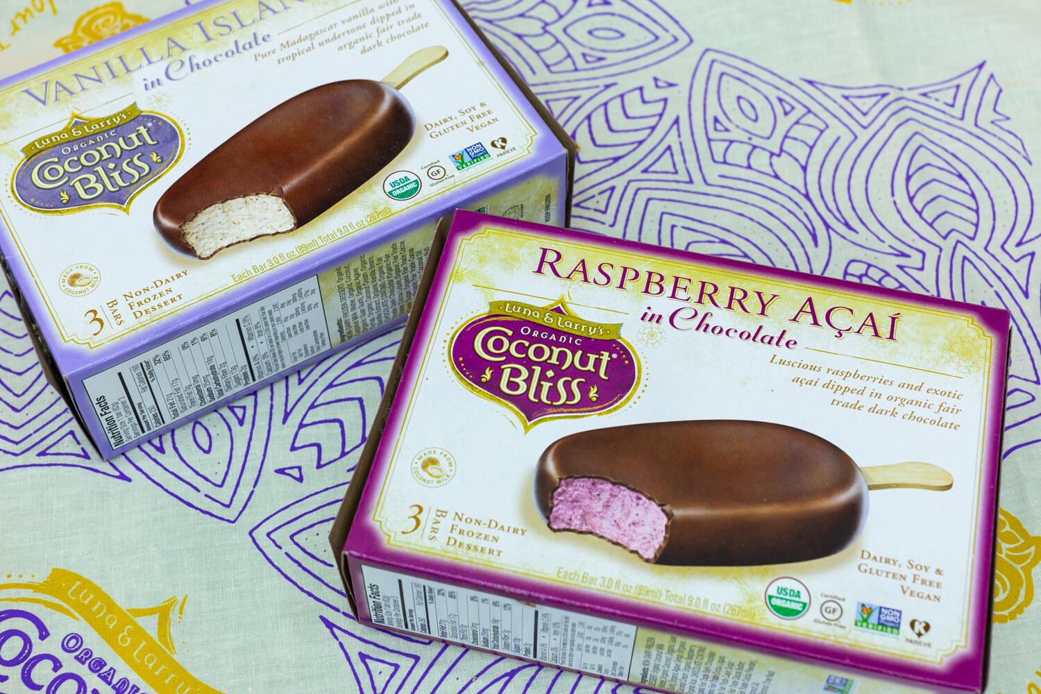 Two boxes of Coconut Bliss chocolate-dipped bars on a patterned tablecloth.