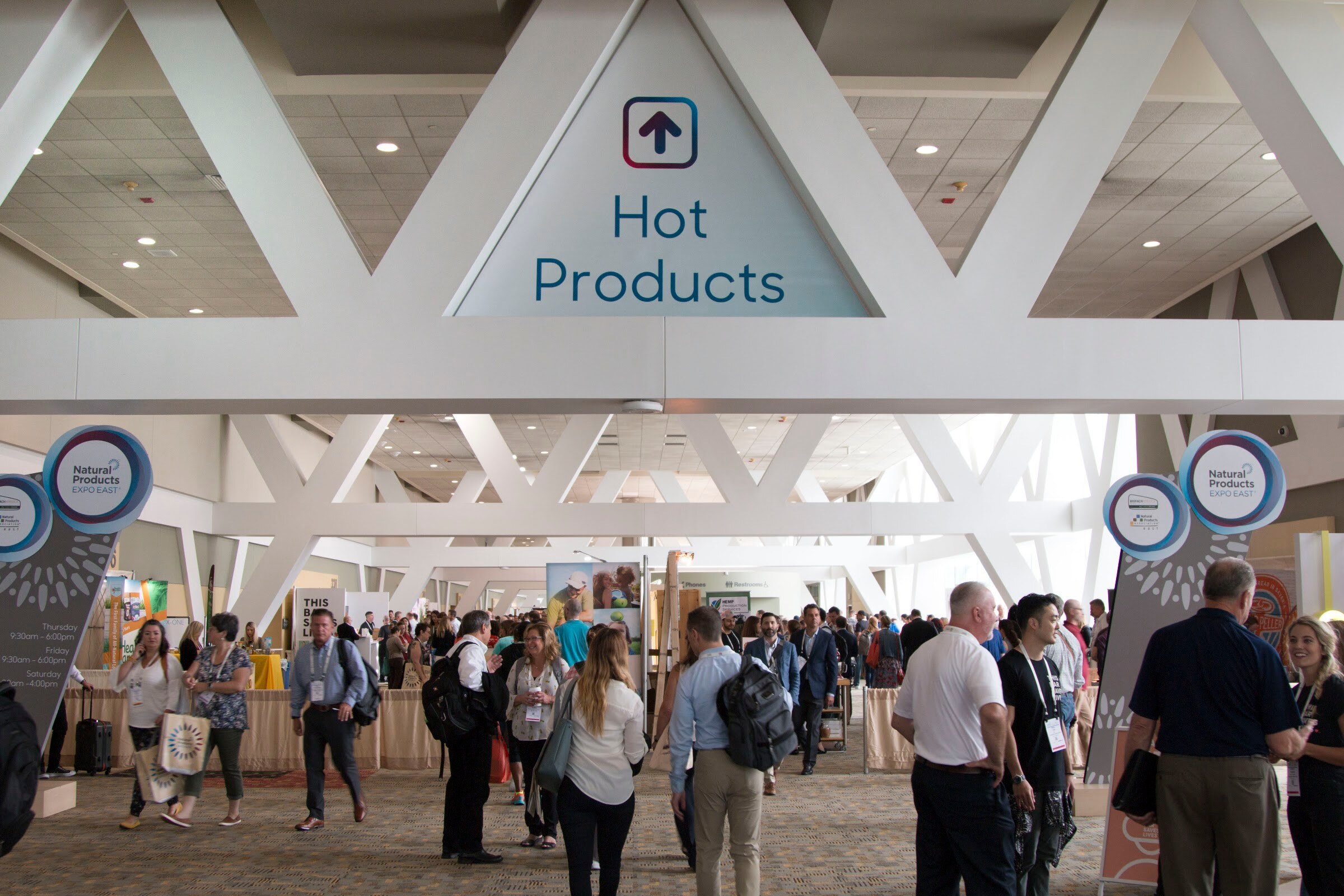 Dozens of attendees with badges under a white lattice ceiling and a Hot Products sign.