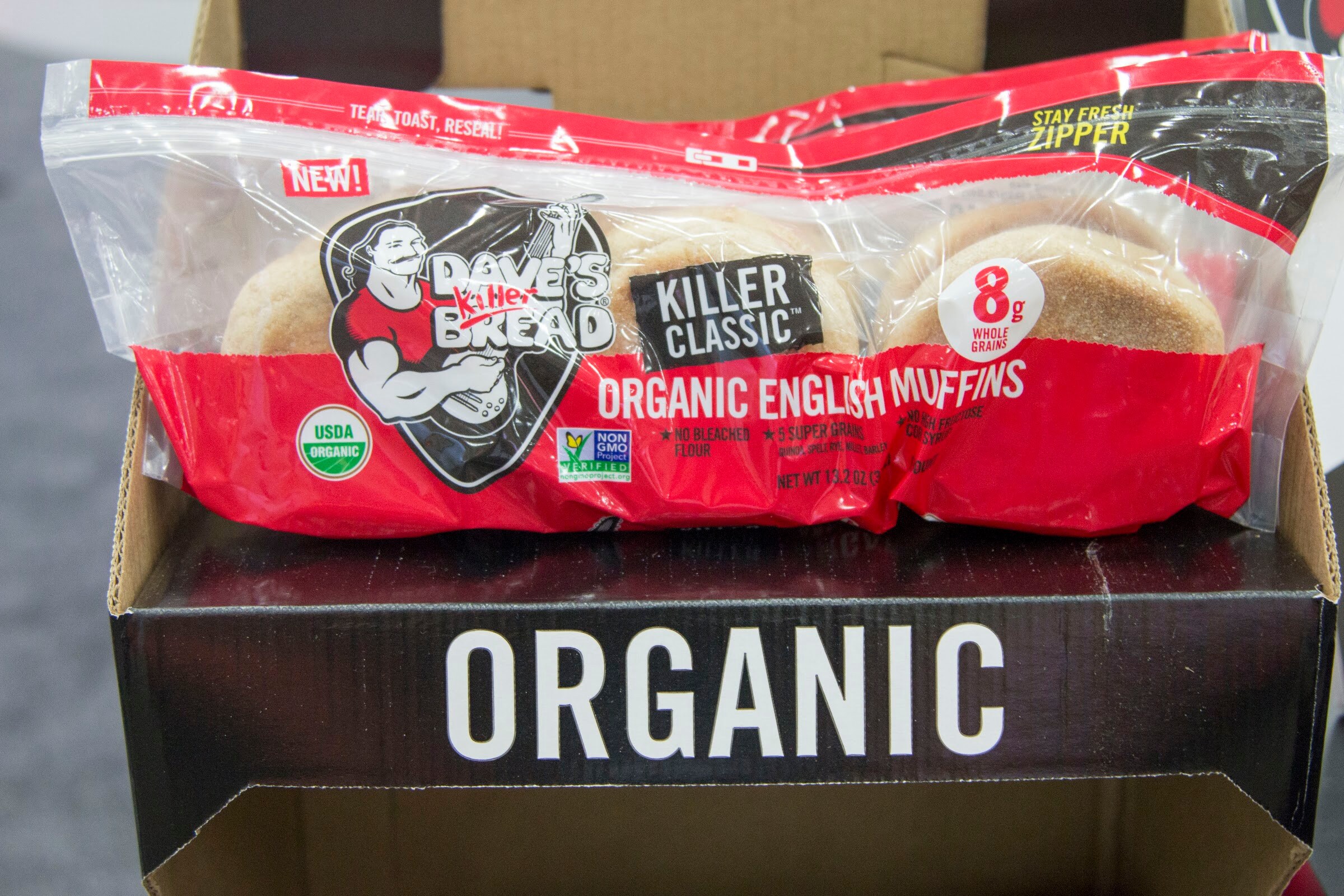 A bag of Dave's Killer Bread organic English muffins sitting on a black box printed Organic.