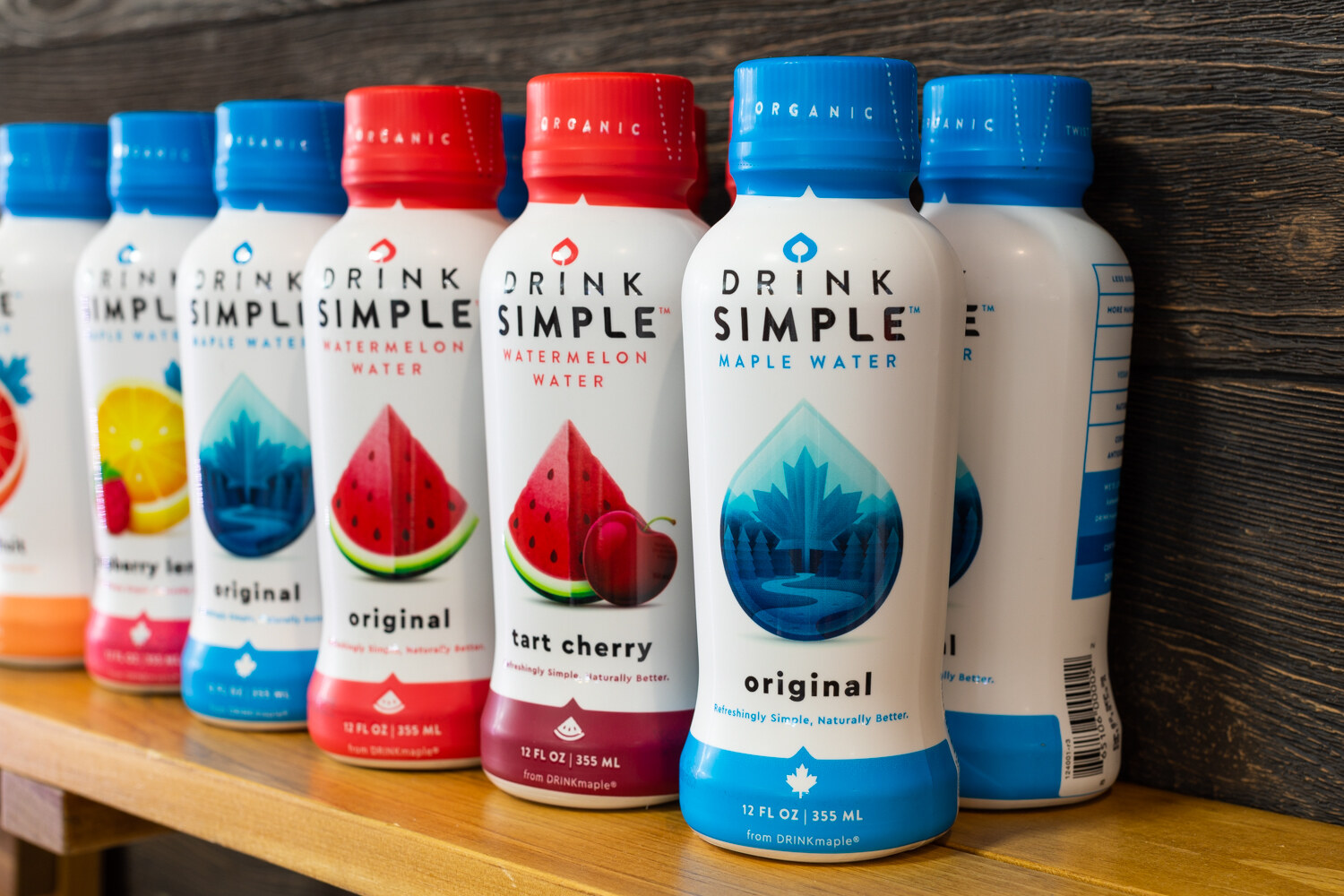 A row of blue and red Drink Simple bottles on a wooden shelf against a dark wood wall.