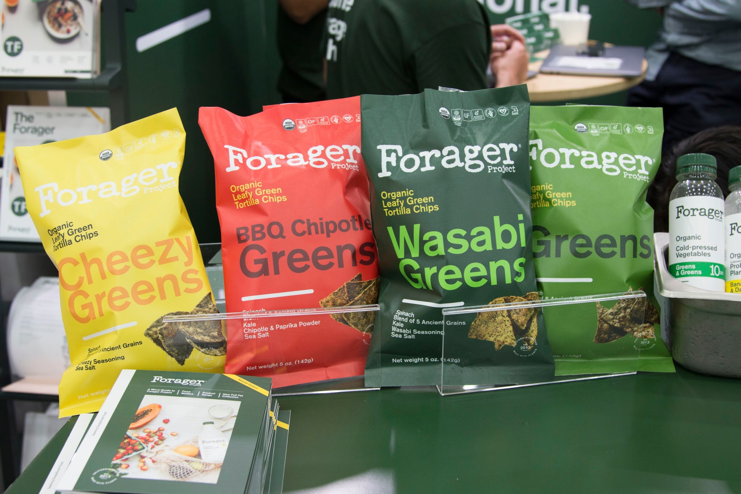 Four bags of Forager Project chips on a green display with bottles of Forager drinks beside them.