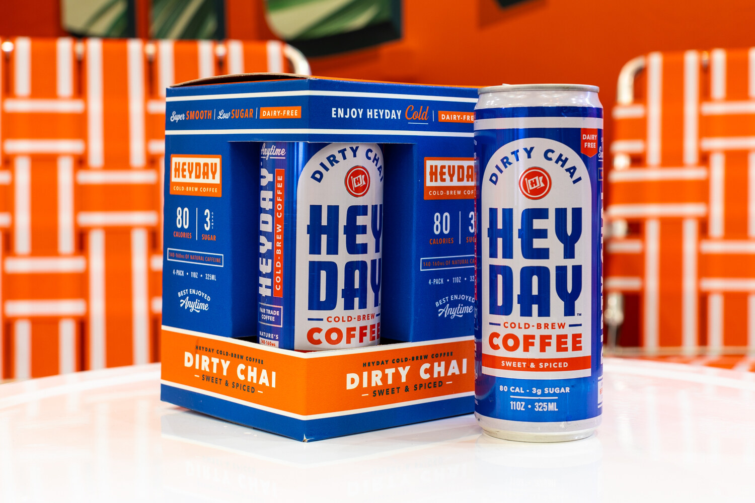 A blue and orange Heyday four-pack beside a single can in front of an orange lawn-chair backdrop.