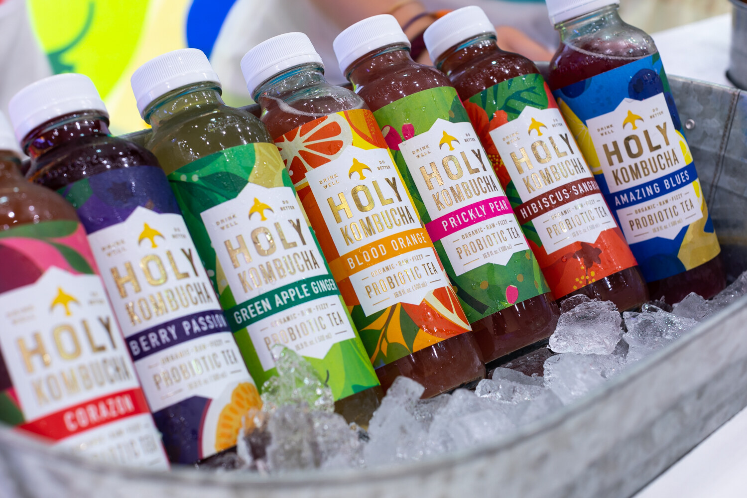 A row of colorful Holy Kombucha bottles lying in ice in a metal tub.