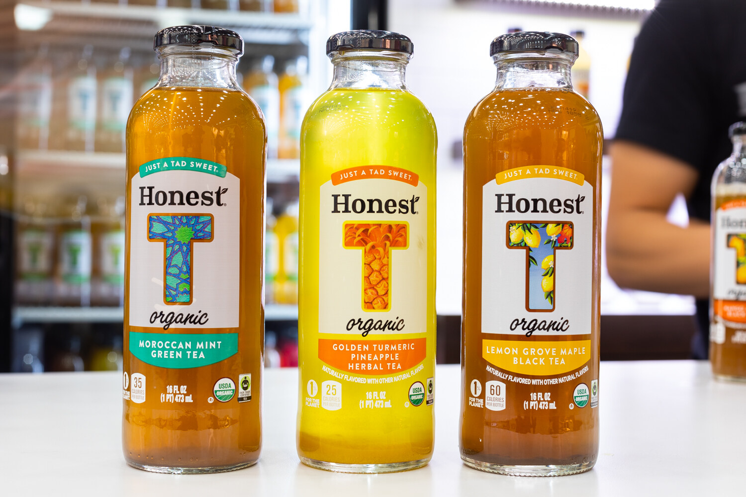 Three glass Honest Tea bottles with yellow, green and orange teas on a white counter.