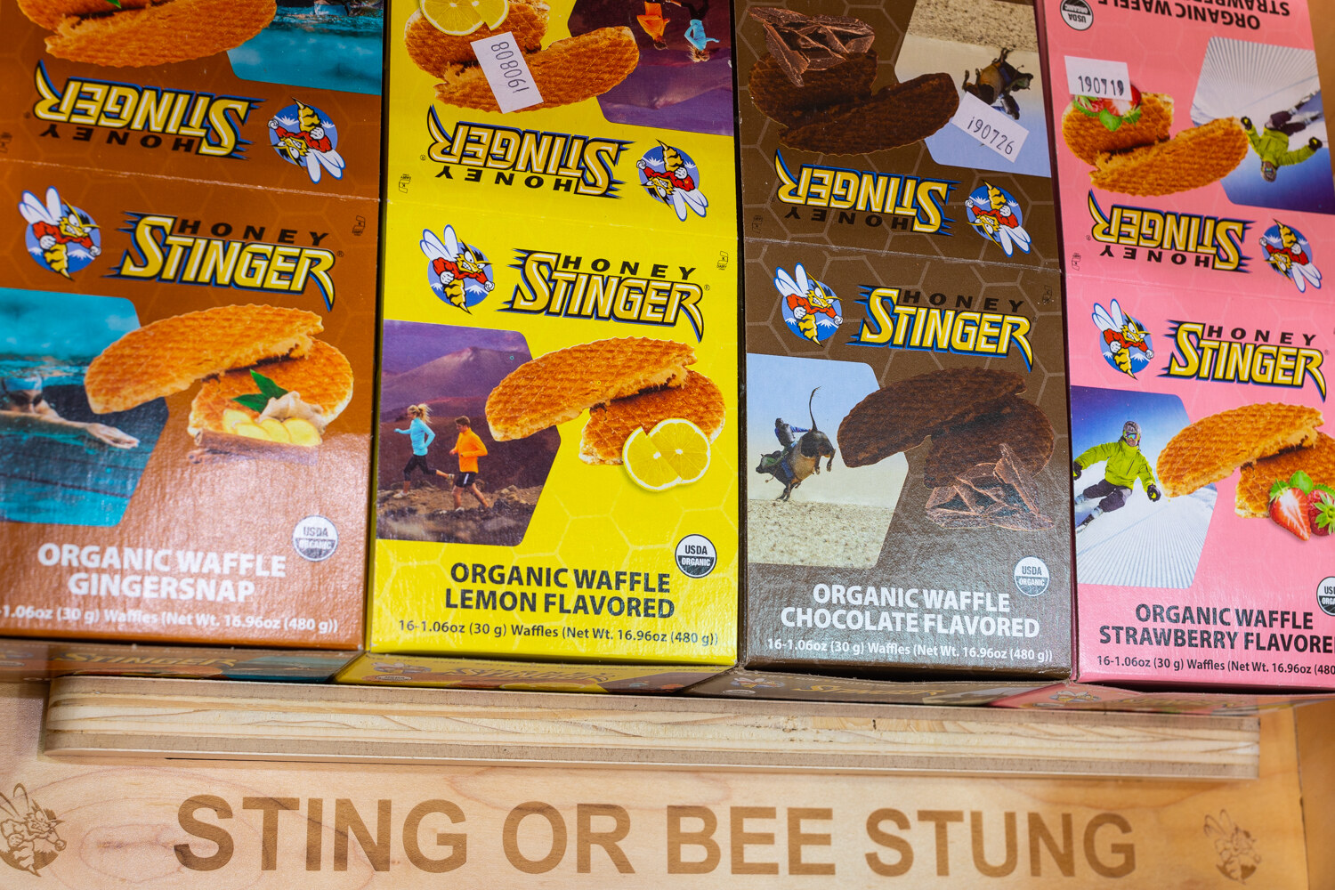 Four colorful Honey Stinger waffle boxes above a wooden crate stamped Sting or Bee Stung.