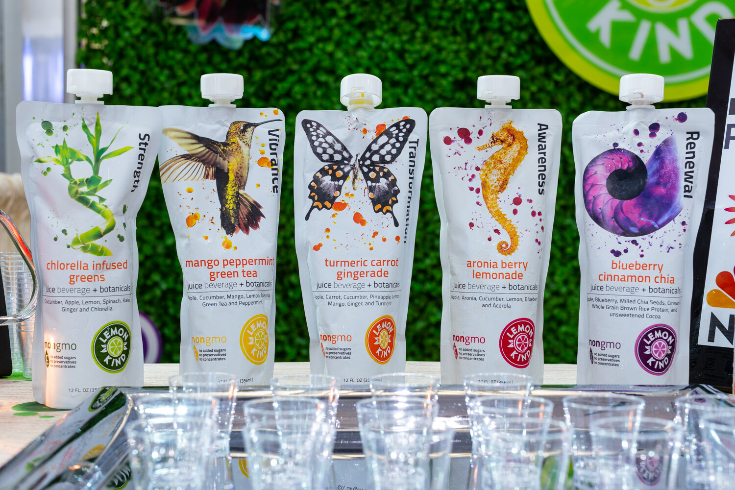 Five white Lemon King pouches with hummingbird, butterfly and seahorse artwork in front of a green wall.