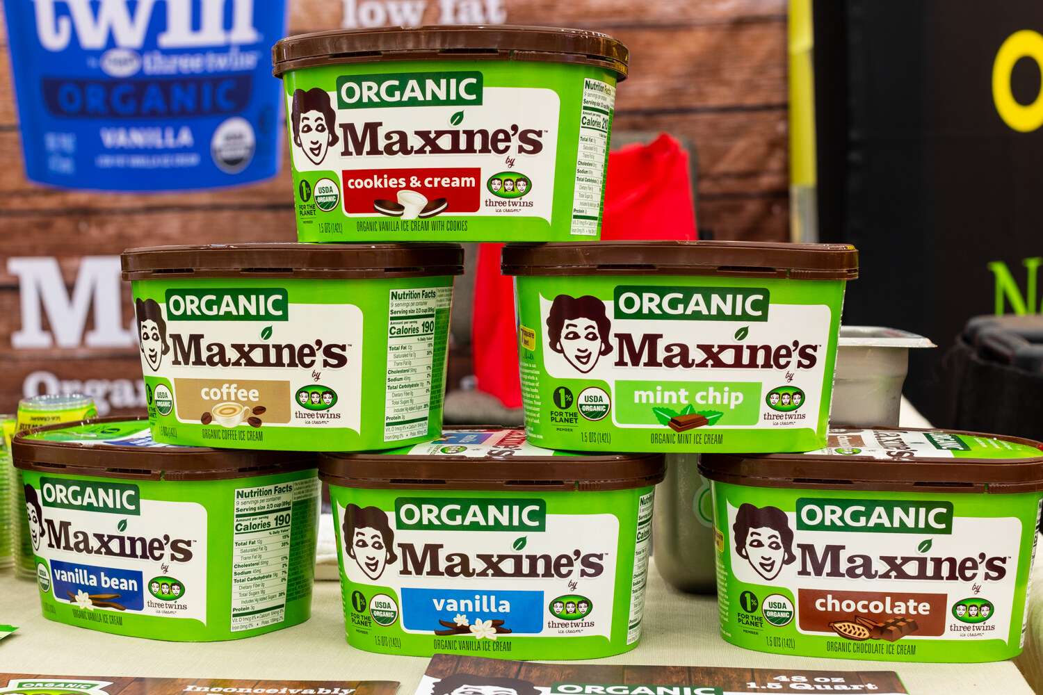 A pyramid of green Maxine's organic ice cream tubs in front of a wooden backdrop.