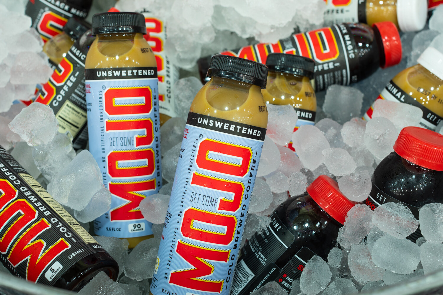 Several Mojo cold-brew coffee bottles with bold red and blue labels in crushed ice.