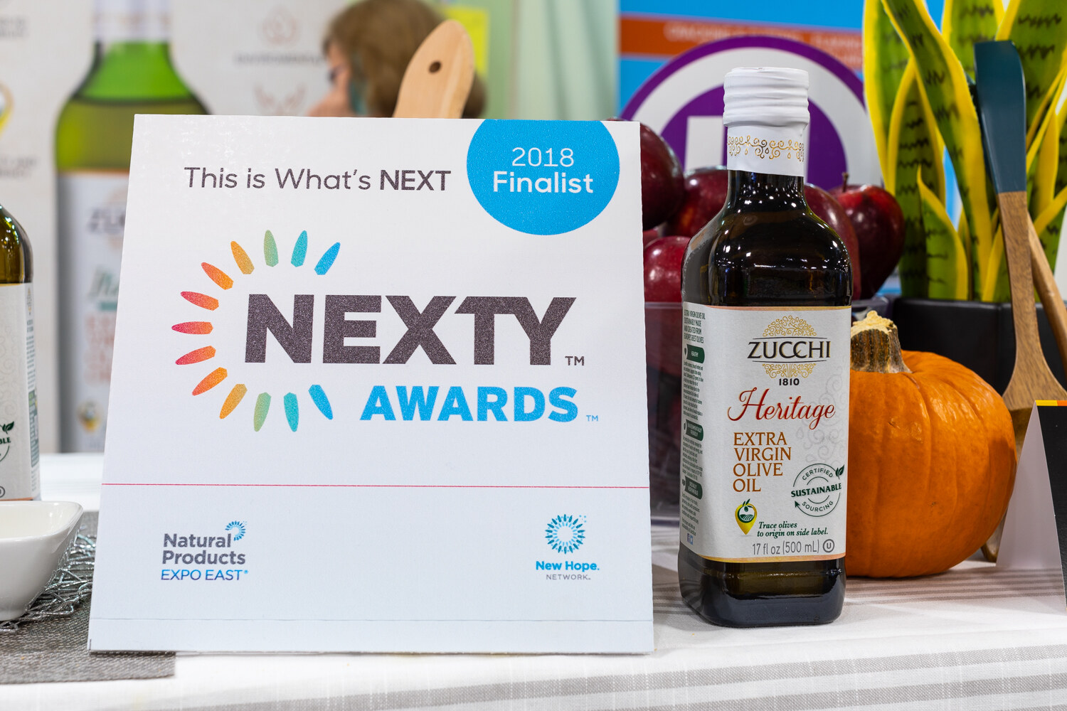 A table sign reading NEXTY Awards 2018 Finalist next to an olive oil bottle and a pumpkin.