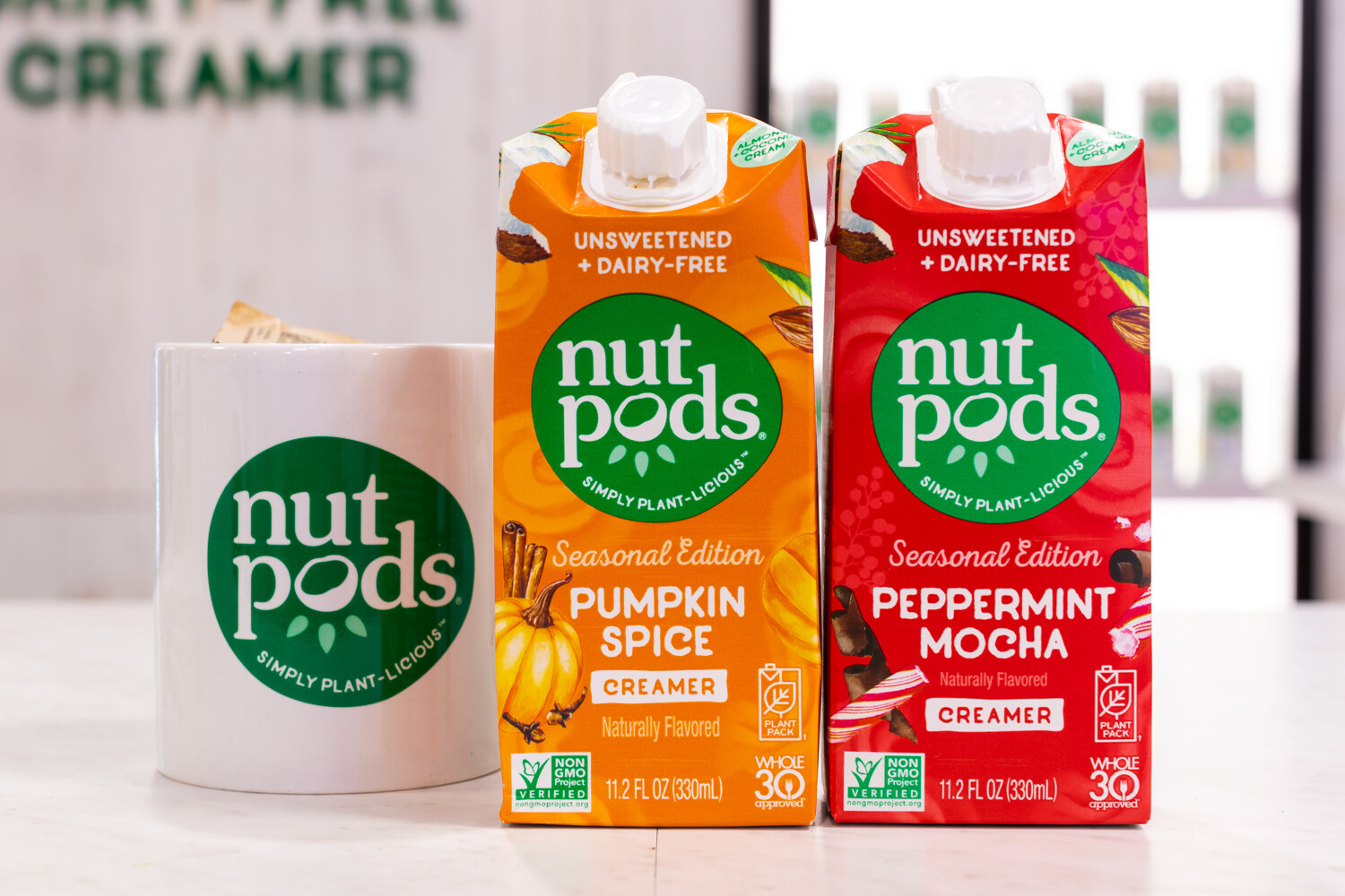 Two orange and red Nutpods creamer cartons next to a white mug with the green nutpods logo.