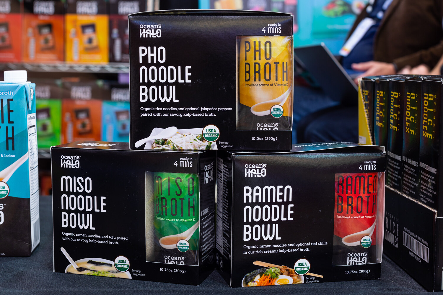 Three black Ocean's Halo noodle bowl boxes stacked on a table with other boxes behind.