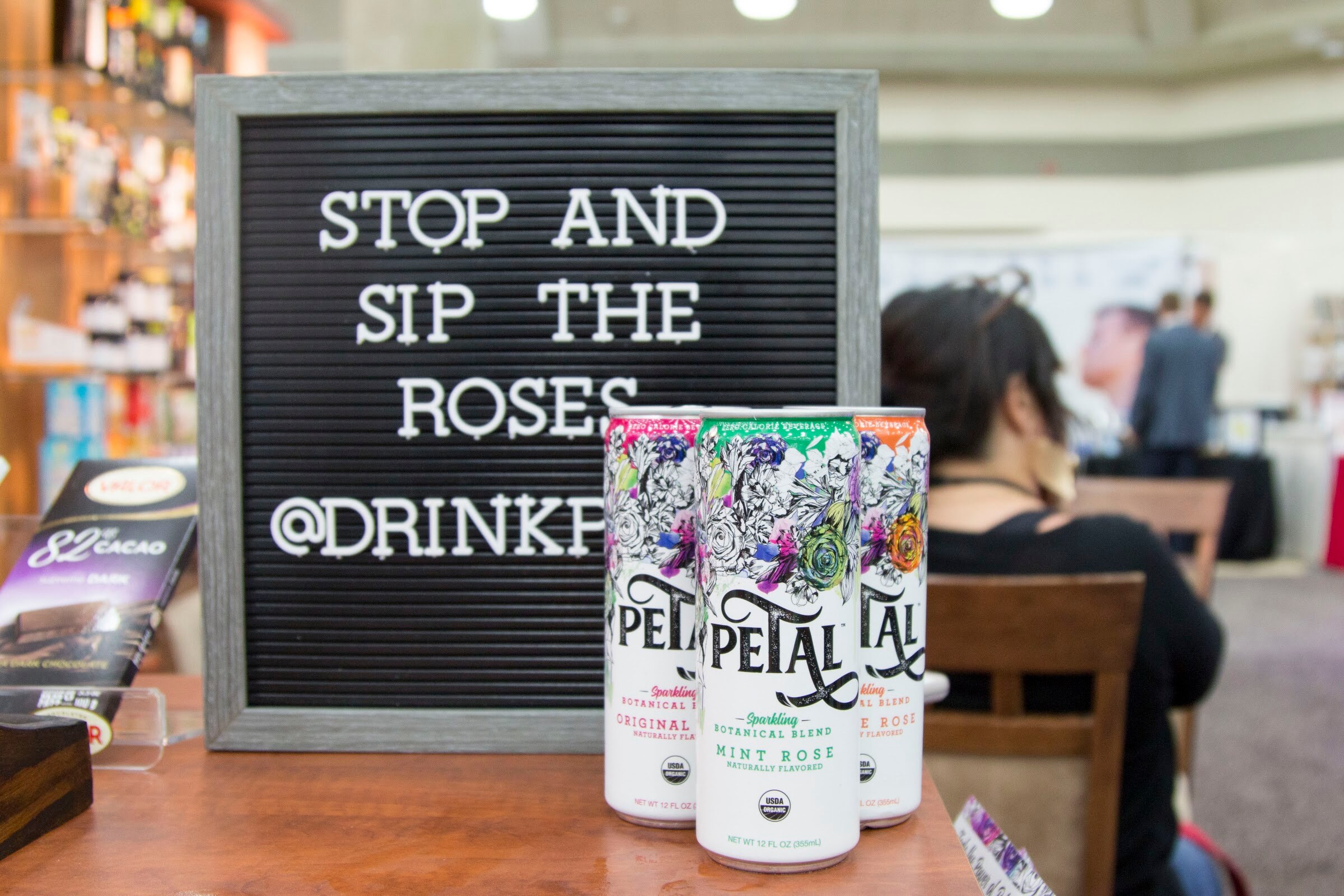 Three Petal cans with floral illustrations in front of a black letterboard sign.