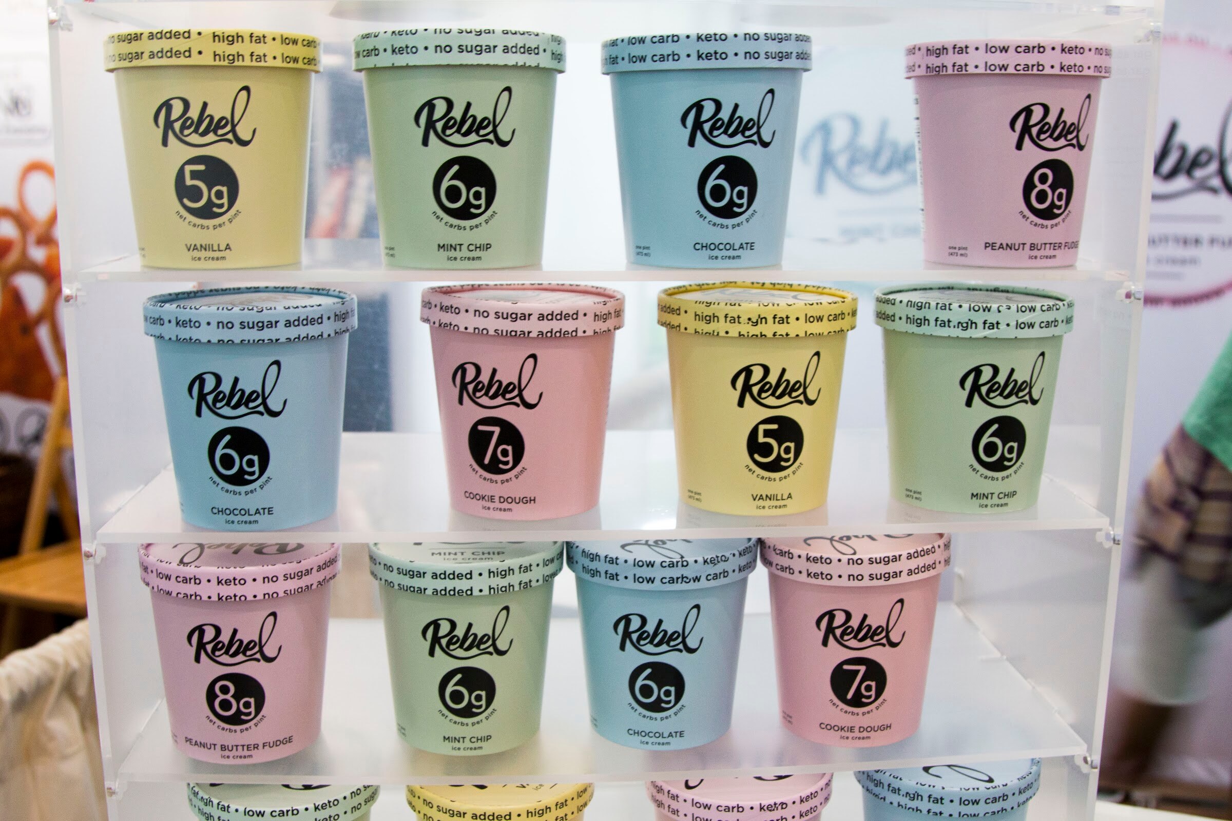 Rows of pastel Rebel pints marked with grams of sugar on clear acrylic shelves.