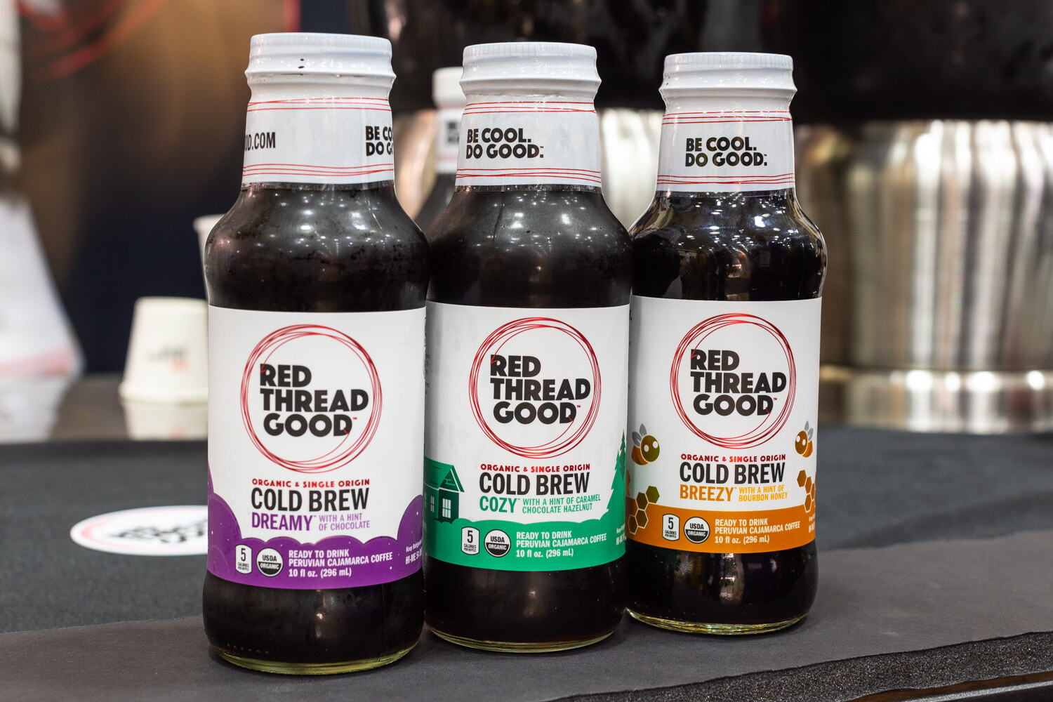 Three dark Red Thread Good bottles with white labels on a black table.