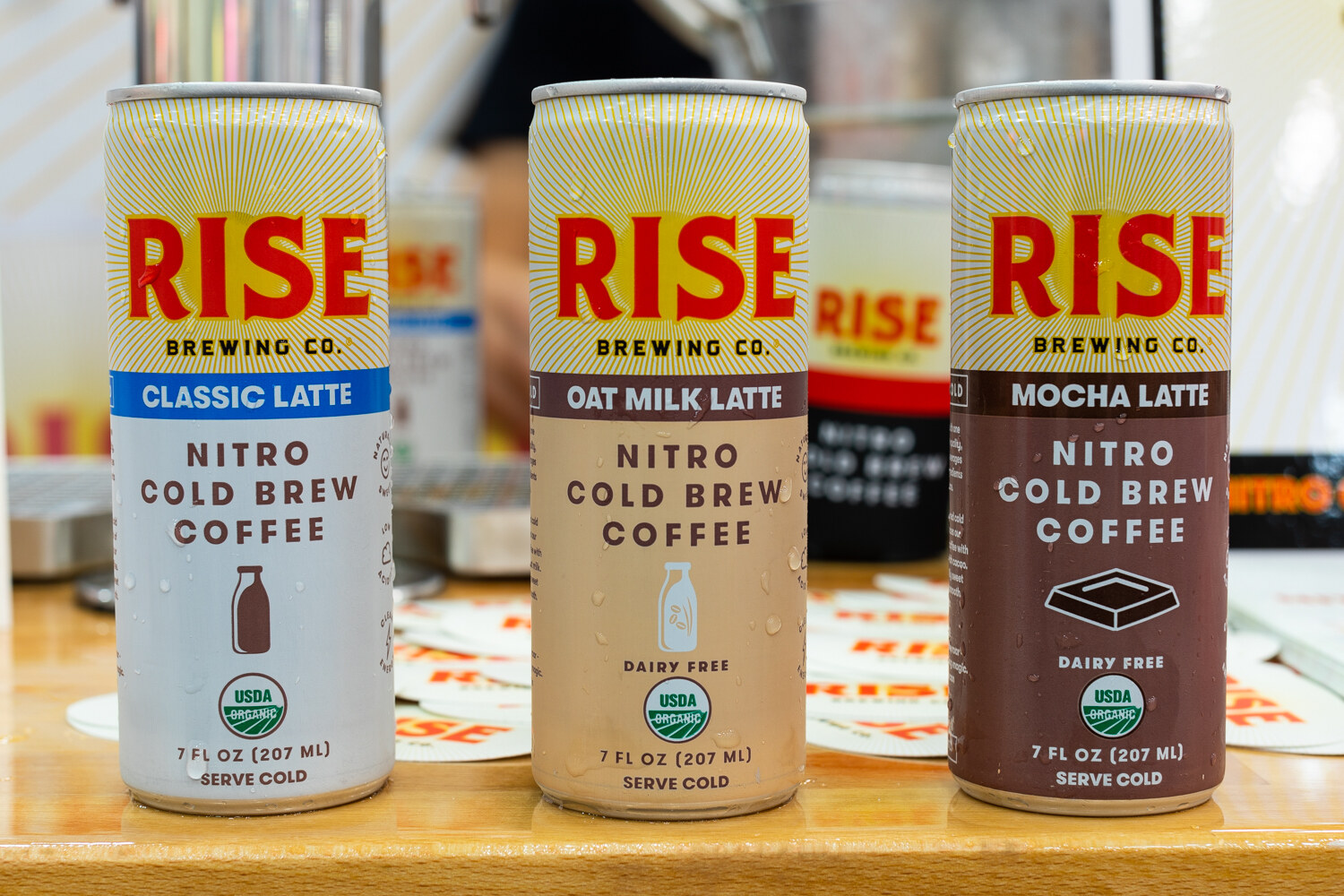 Three Rise Brewing Co. cans with red lettering on a wooden counter.