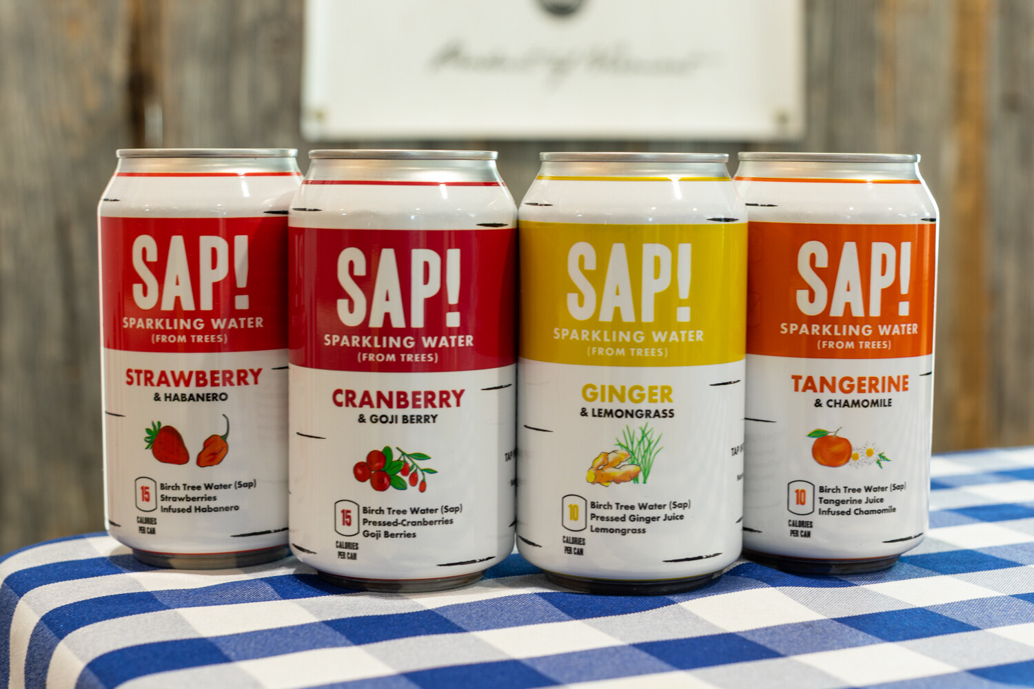 Four SAP! cans in red, yellow and orange on a blue-and-white checkered tablecloth.