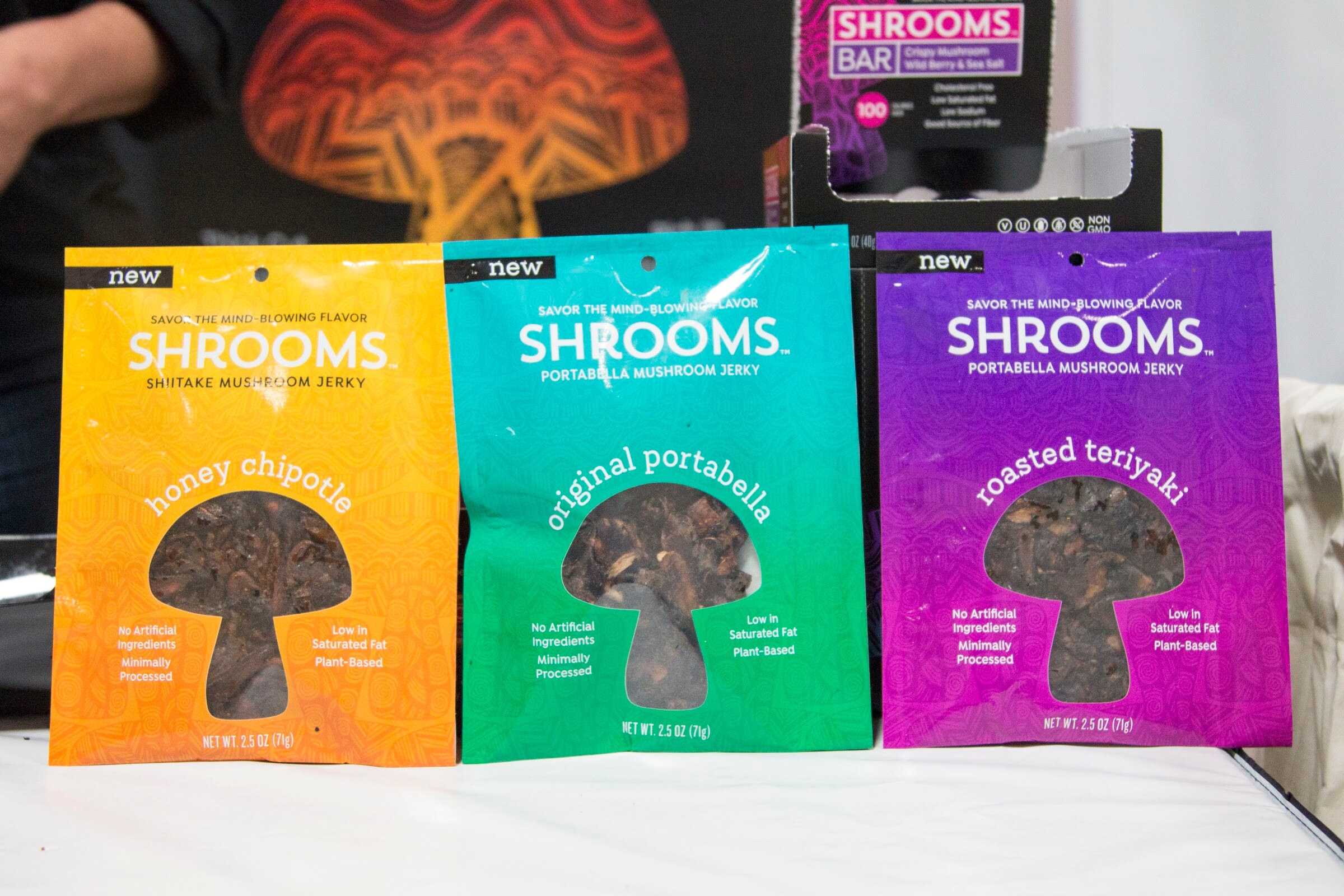 Three colorful Shrooms jerky bags with mushroom-shaped windows on a white table.