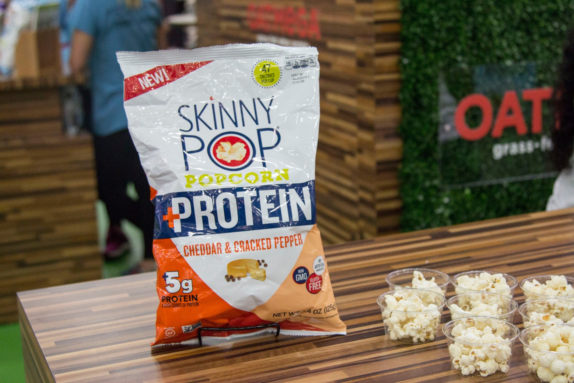 A bag of Skinny Pop protein popcorn on a wood counter beside cups of popcorn.