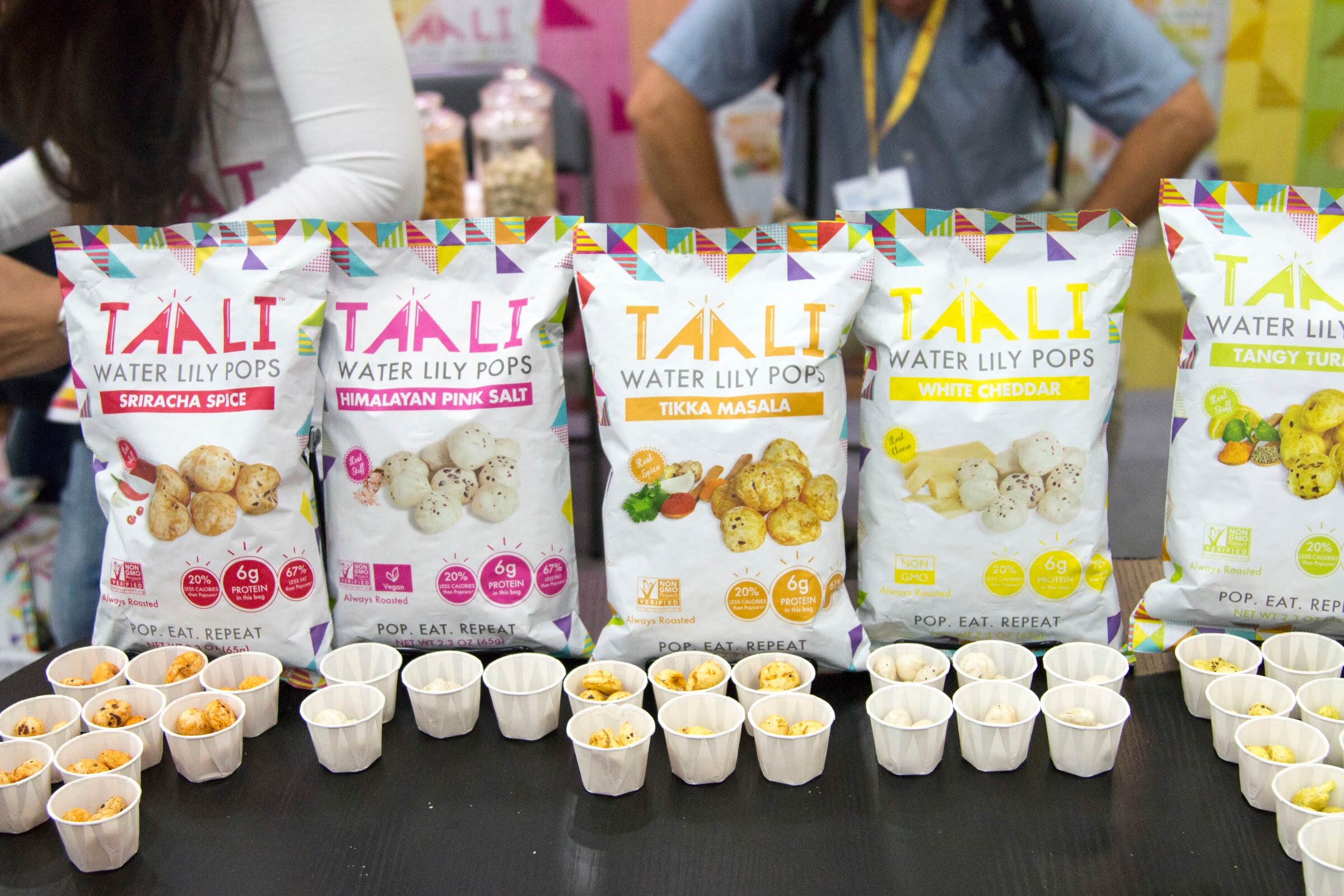 Five bags of Taali popped water lily seeds above rows of small paper sample cups.