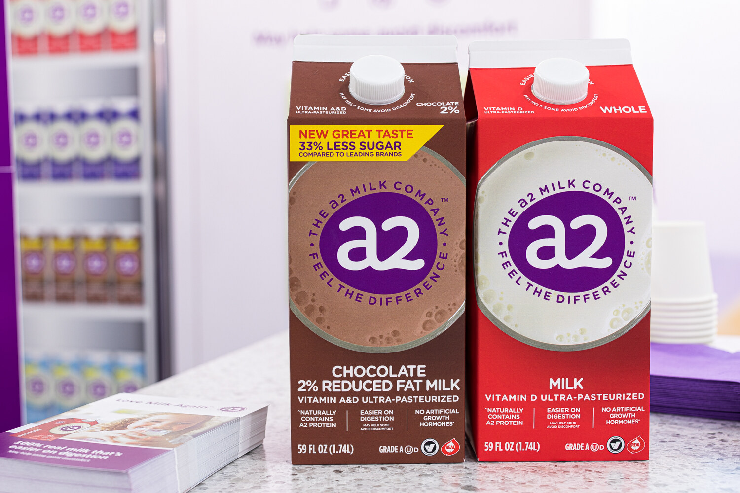 Two a2 Milk cartons, one chocolate 2% reduced fat and one whole milk, on a white counter.
