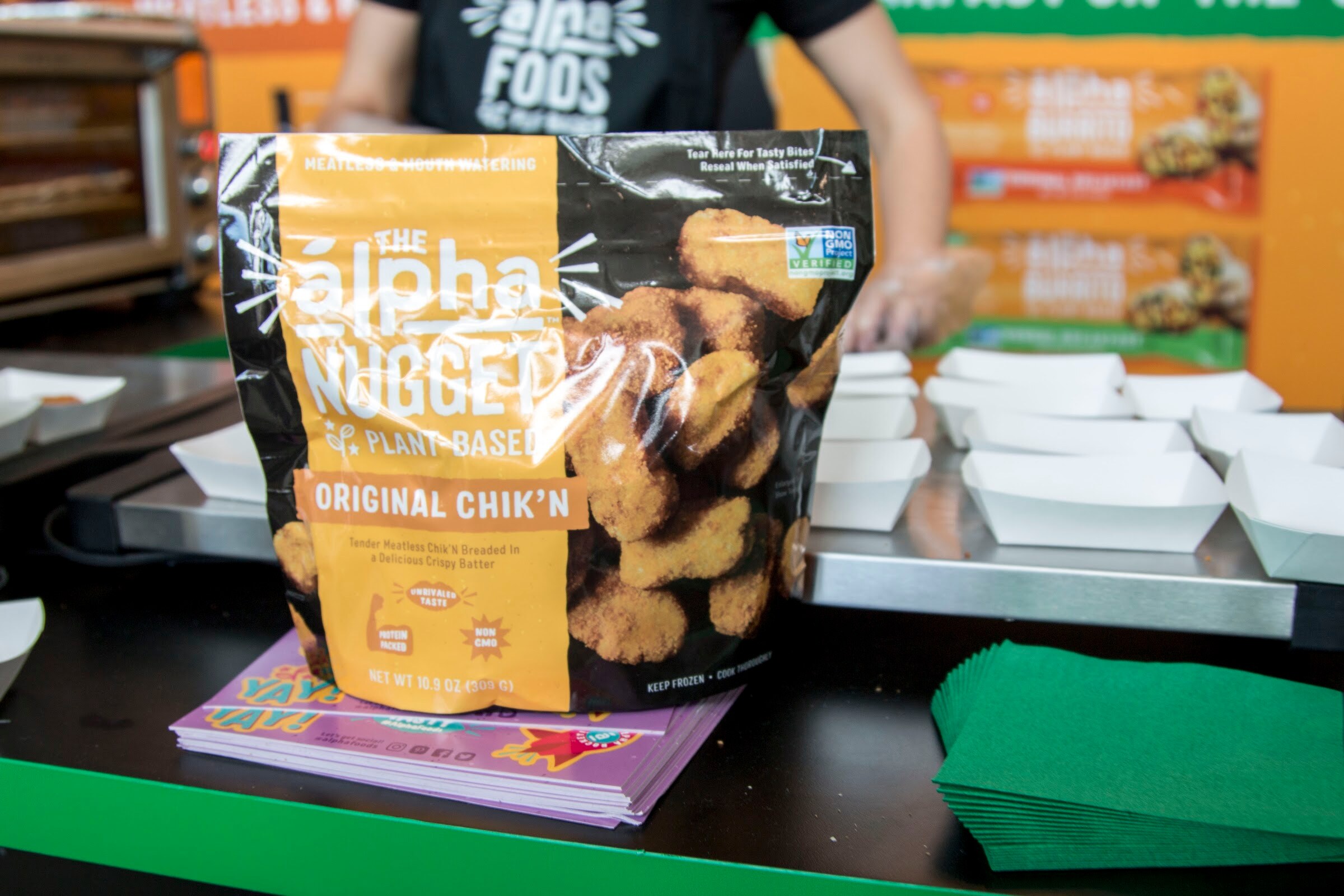 A bag of Alpha Nugget Original Chik'n on a counter with serving trays and green napkins behind it.