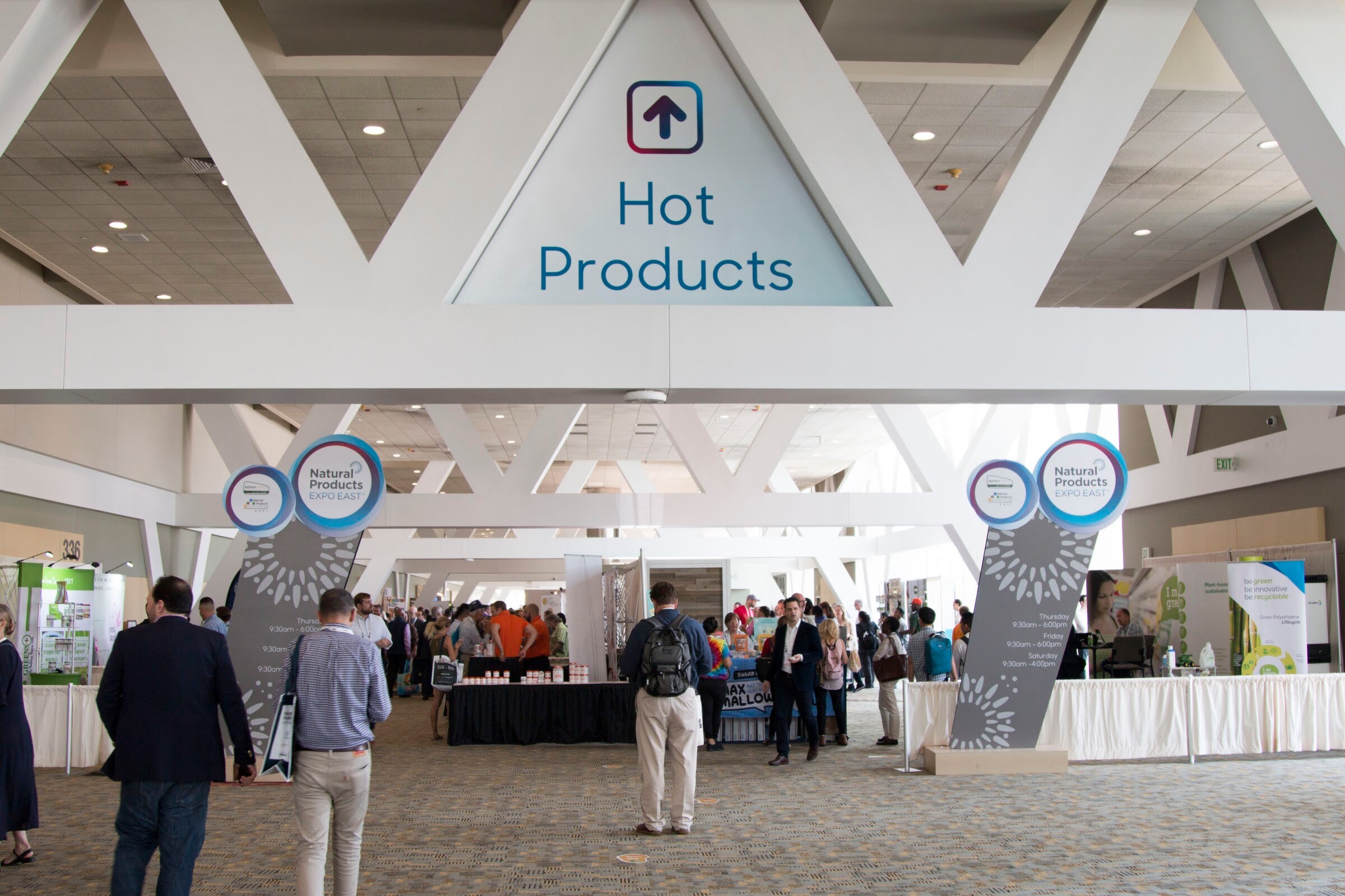 A wide hall with a Hot Products sign overhead and people walking toward exhibitor booths.