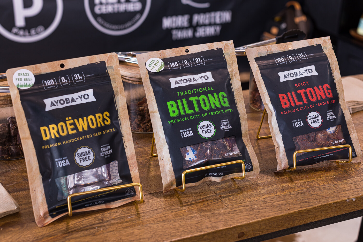 Three bags of Ayoba-Yo biltong in Droewors, Traditional Biltong and Spicy Biltong on a wooden table.