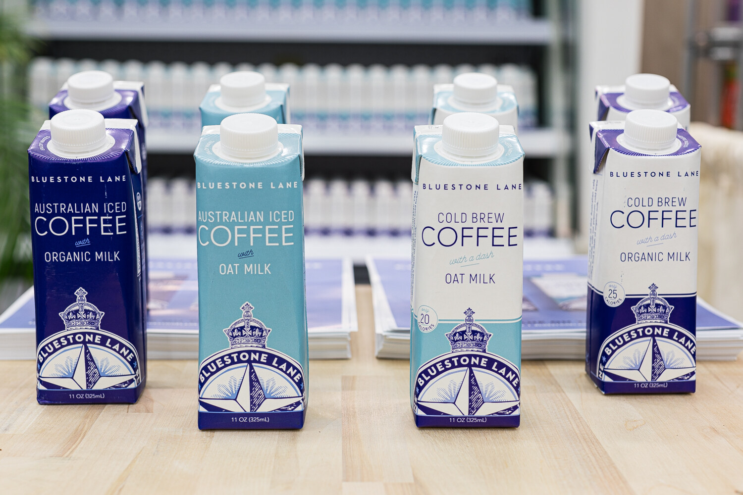 Cartons labeled Bluestone Lane Australian Iced Coffee and Cold Brew Coffee on a light wood table.
