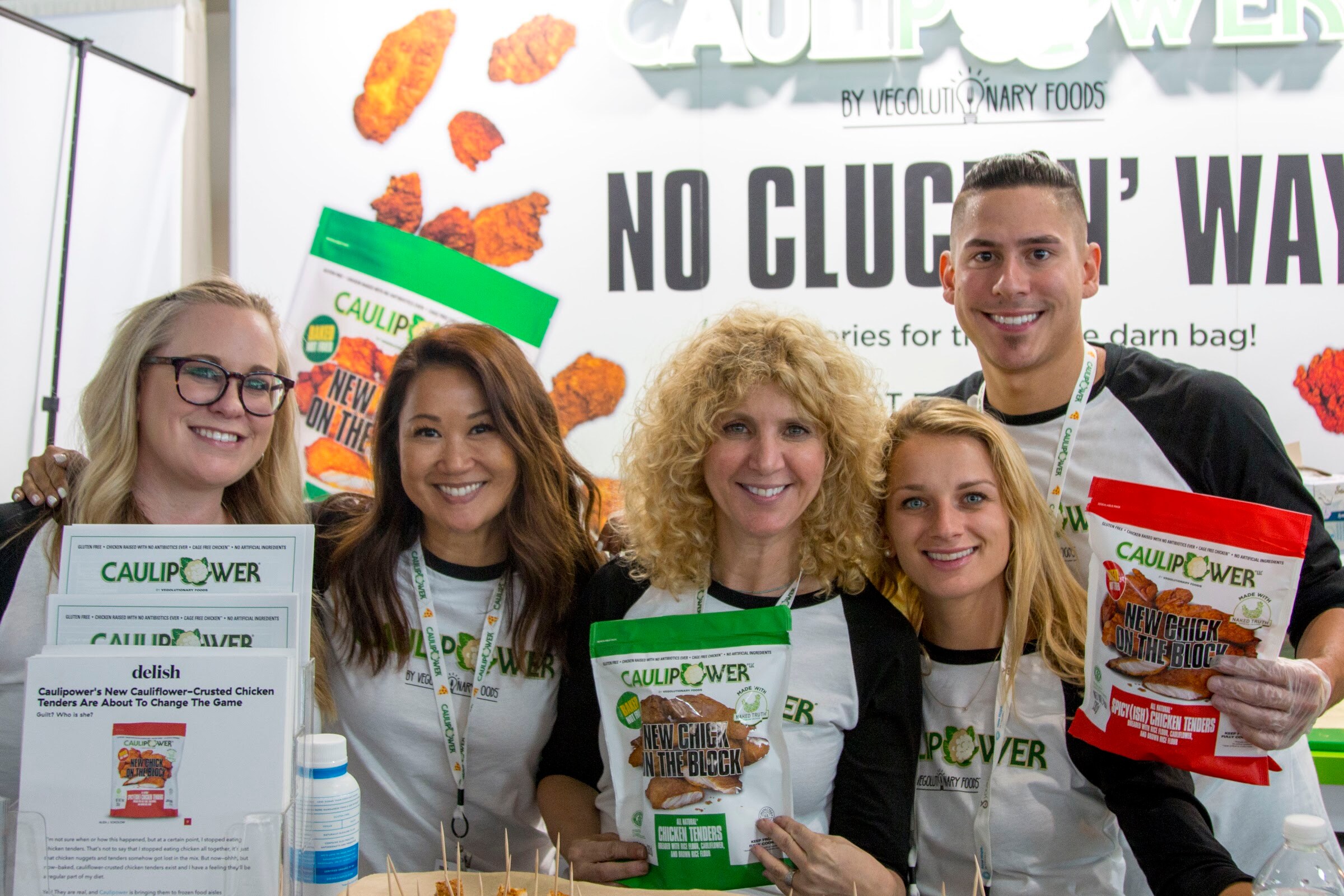 Five smiling people in matching shirts holding Caulipower bags in front of a No Cluckin' Way sign.