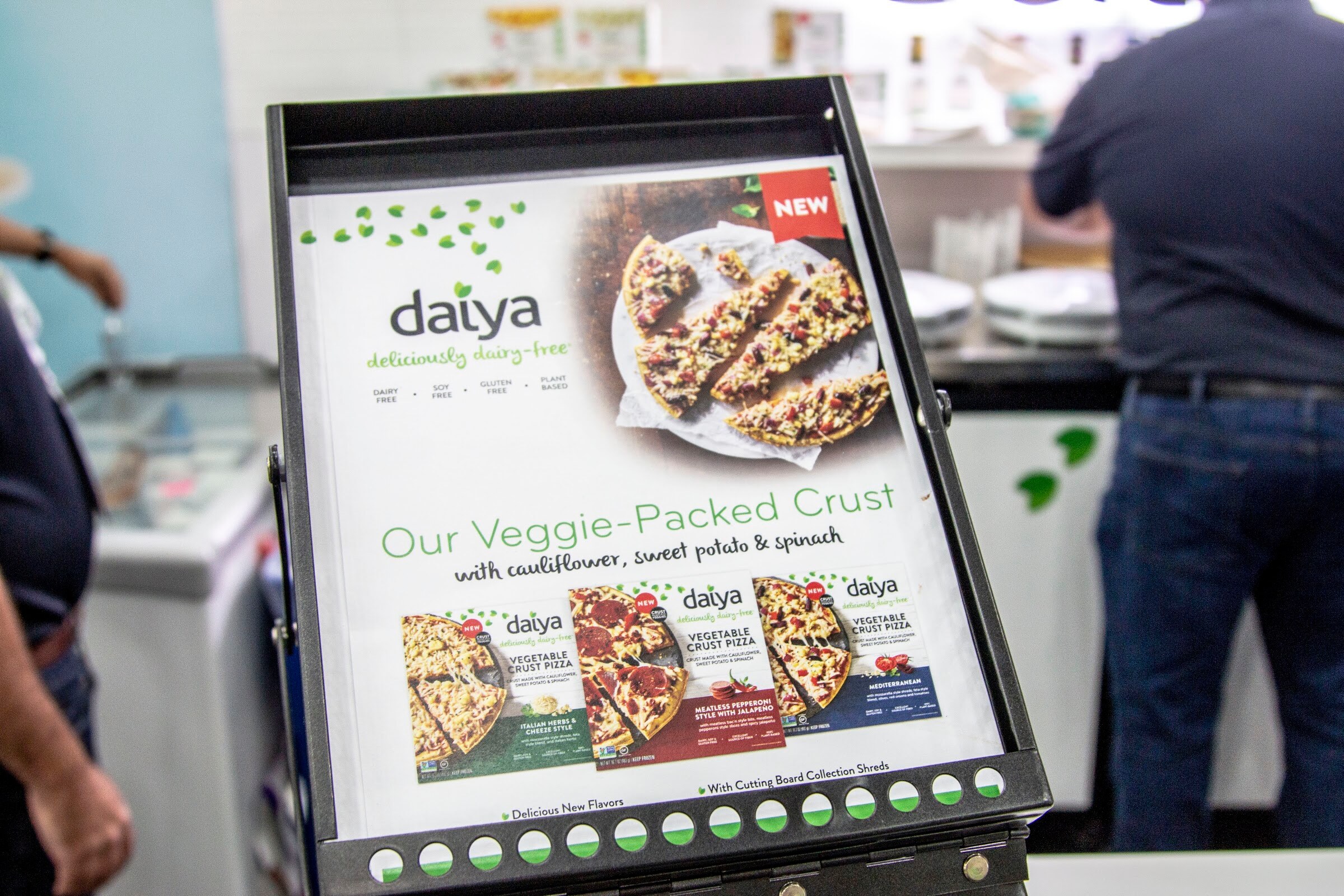 An easel-style sign for Daiya showing pizza slices and the words Our Veggie-Packed Crust.