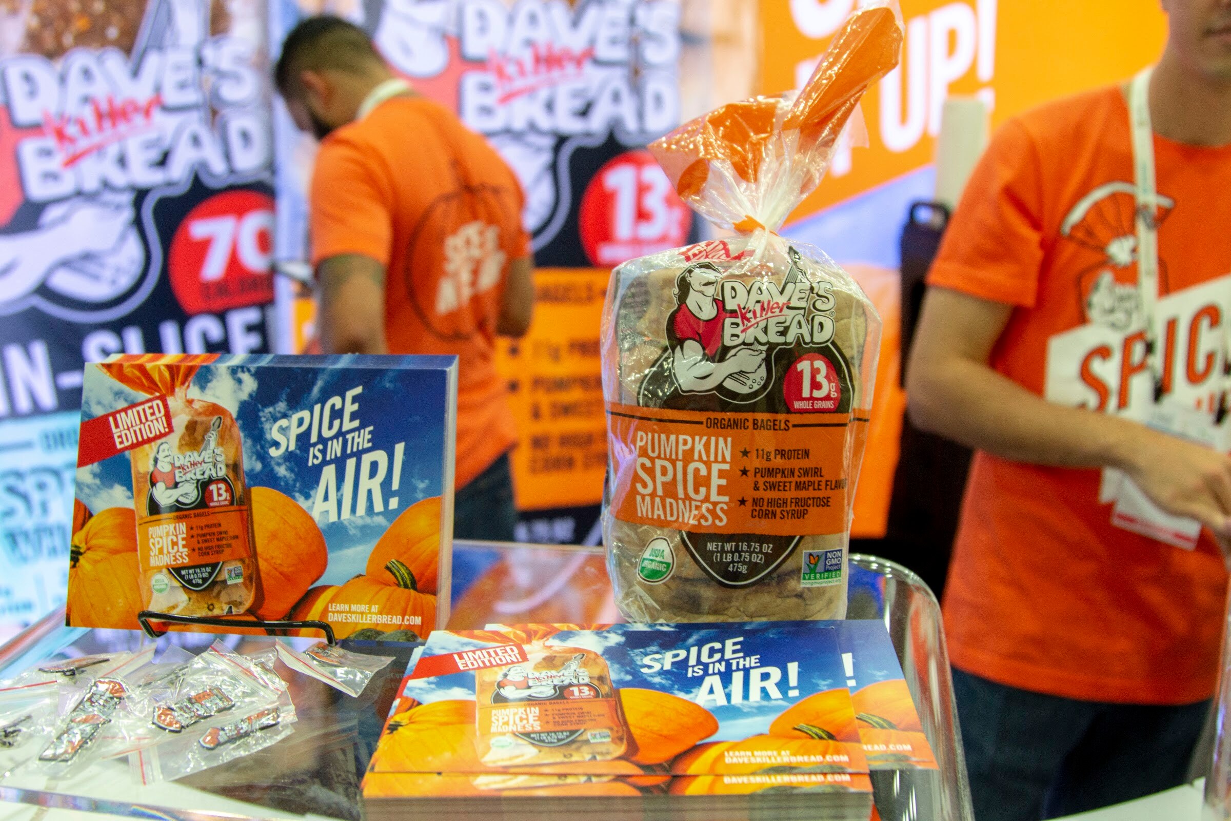 A loaf of Dave's Killer Bread Pumpkin Spice Madness in front of an orange Spice is in the Air sign, with a staffer in orange behind.