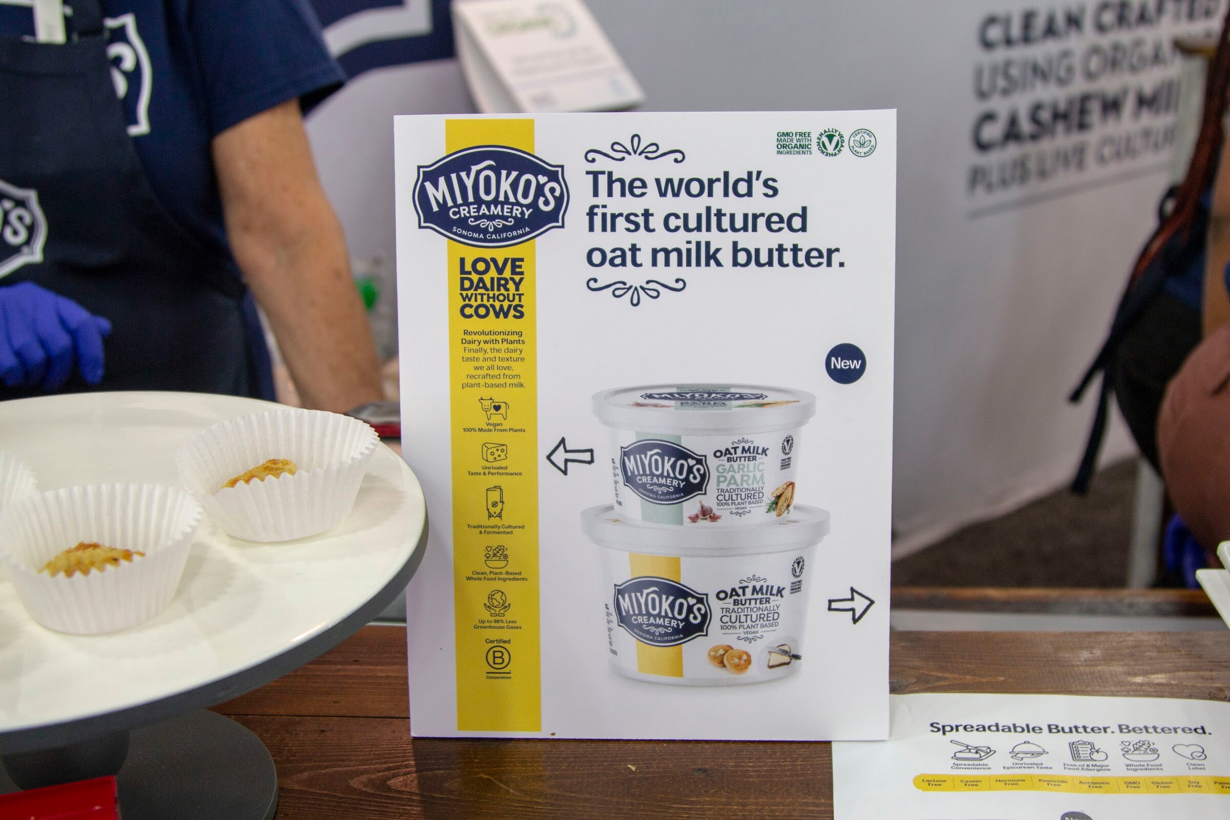 A Miyoko's Creamery display card with product tubs and tasting cups on a counter.