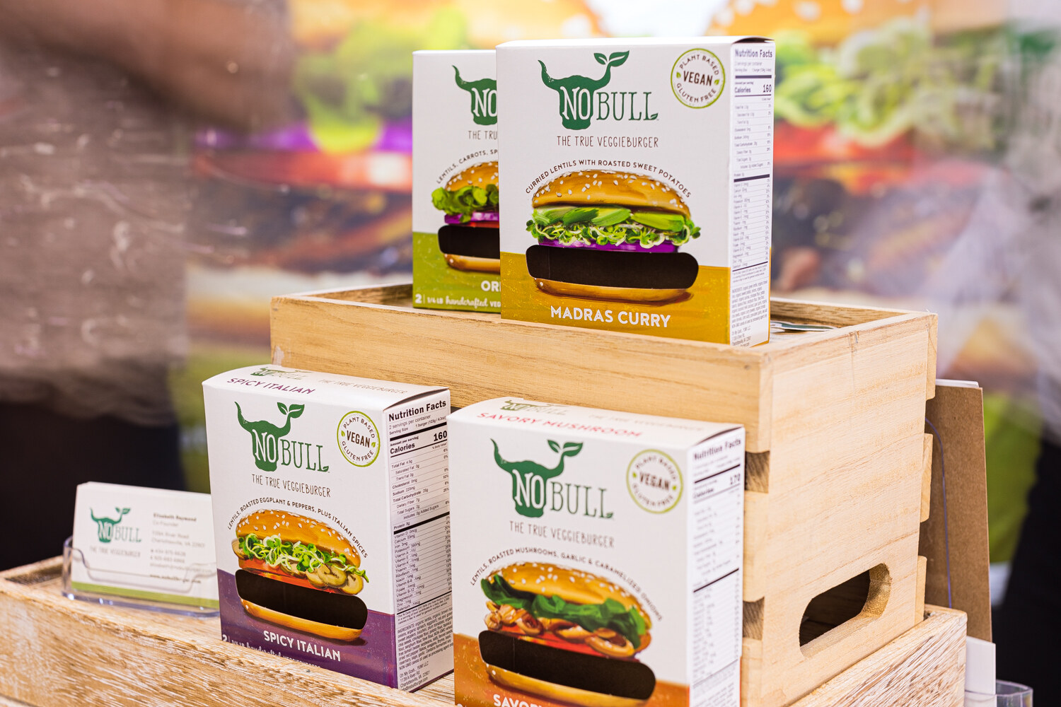 Boxes of NOBULL The True Veggieburger in Madras Curry, Spicy Italian and other flavors on a wooden crate.
