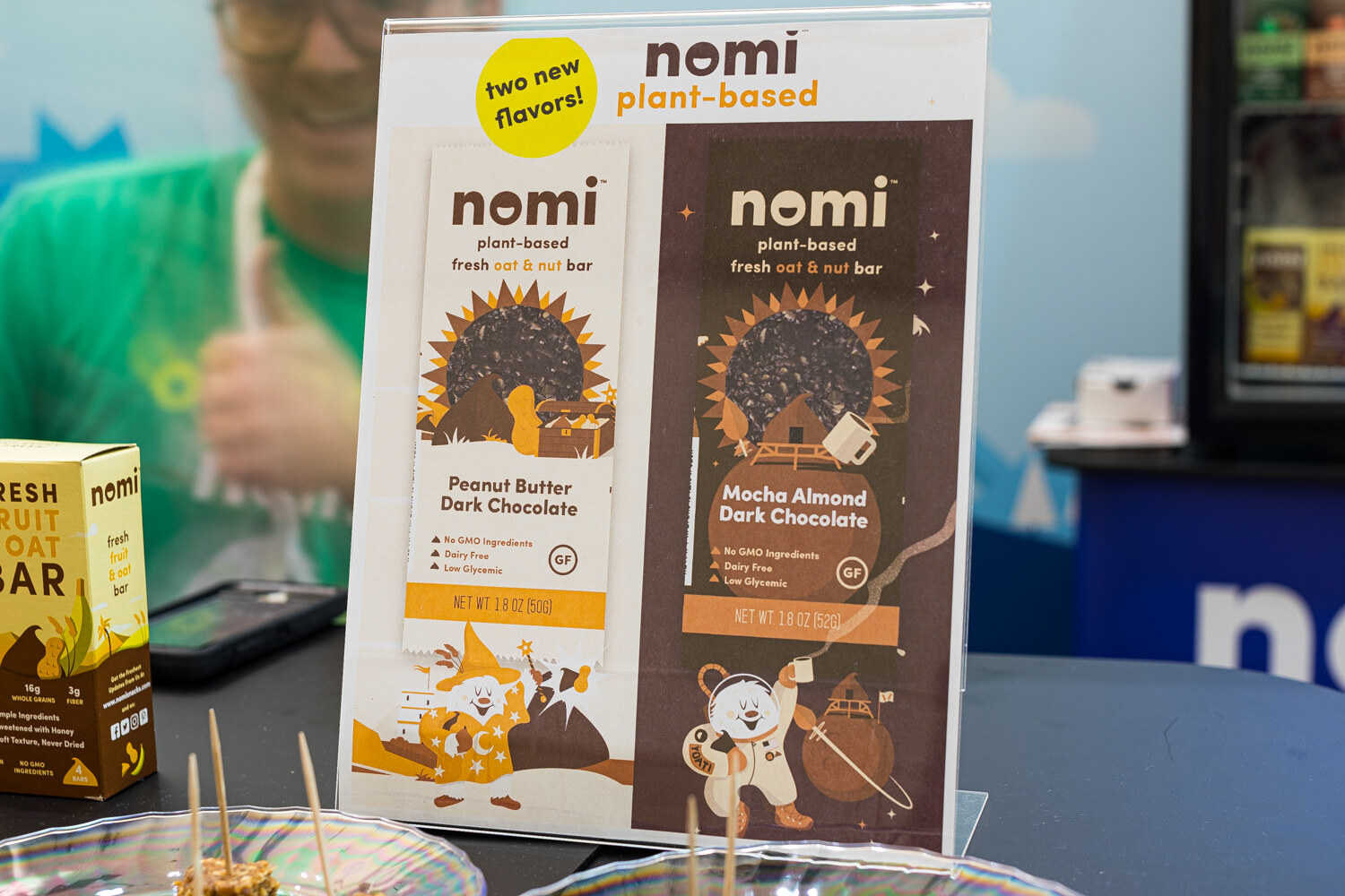 A sign reading nomi plant-based with two new flavors, Peanut Butter Dark Chocolate and Mocha Almond Dark Chocolate.