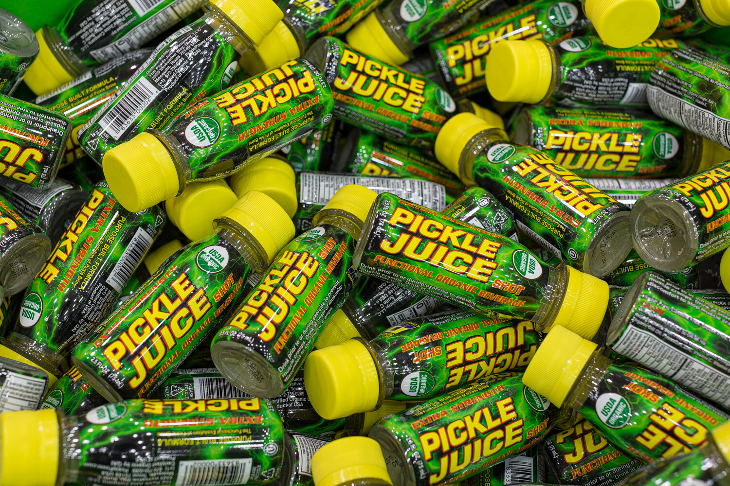 Many green Pickle Juice bottles with yellow caps heaped together.