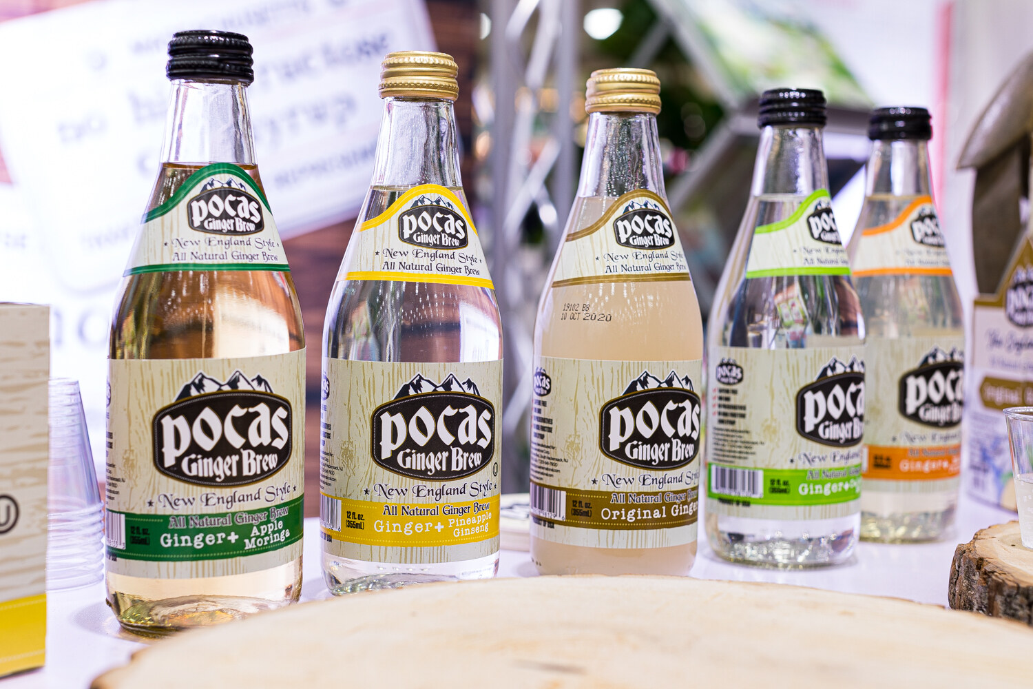 Glass bottles of Pocas Ginger Brew with different colored labels on a wood slice.