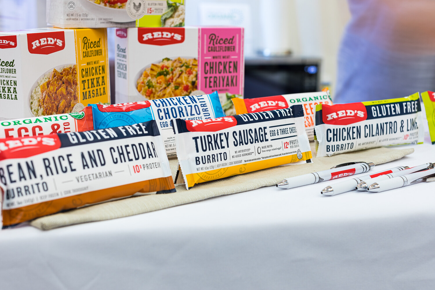 Packages of Red's burritos in bean rice and cheddar, turkey sausage and chicken cilantro lime flavors on a white table.