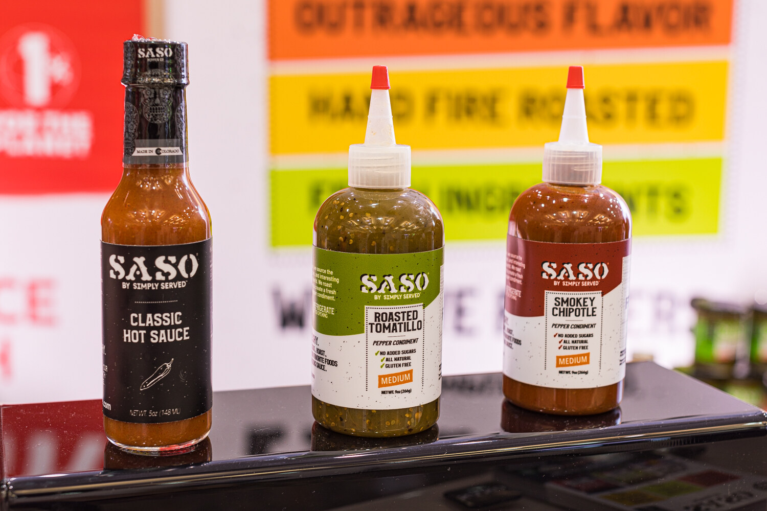 Three bottles of SASO hot sauce with colorful labels on a dark counter.
