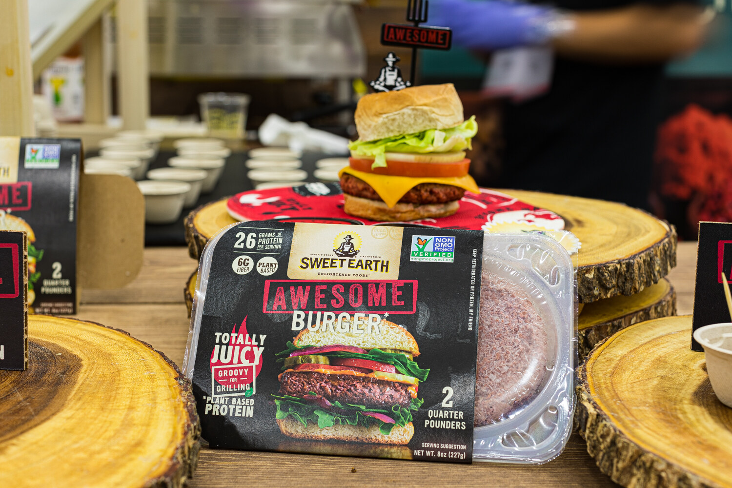 A Sweet Earth Awesome Burger package in front of a cooked burger on a wood slice.