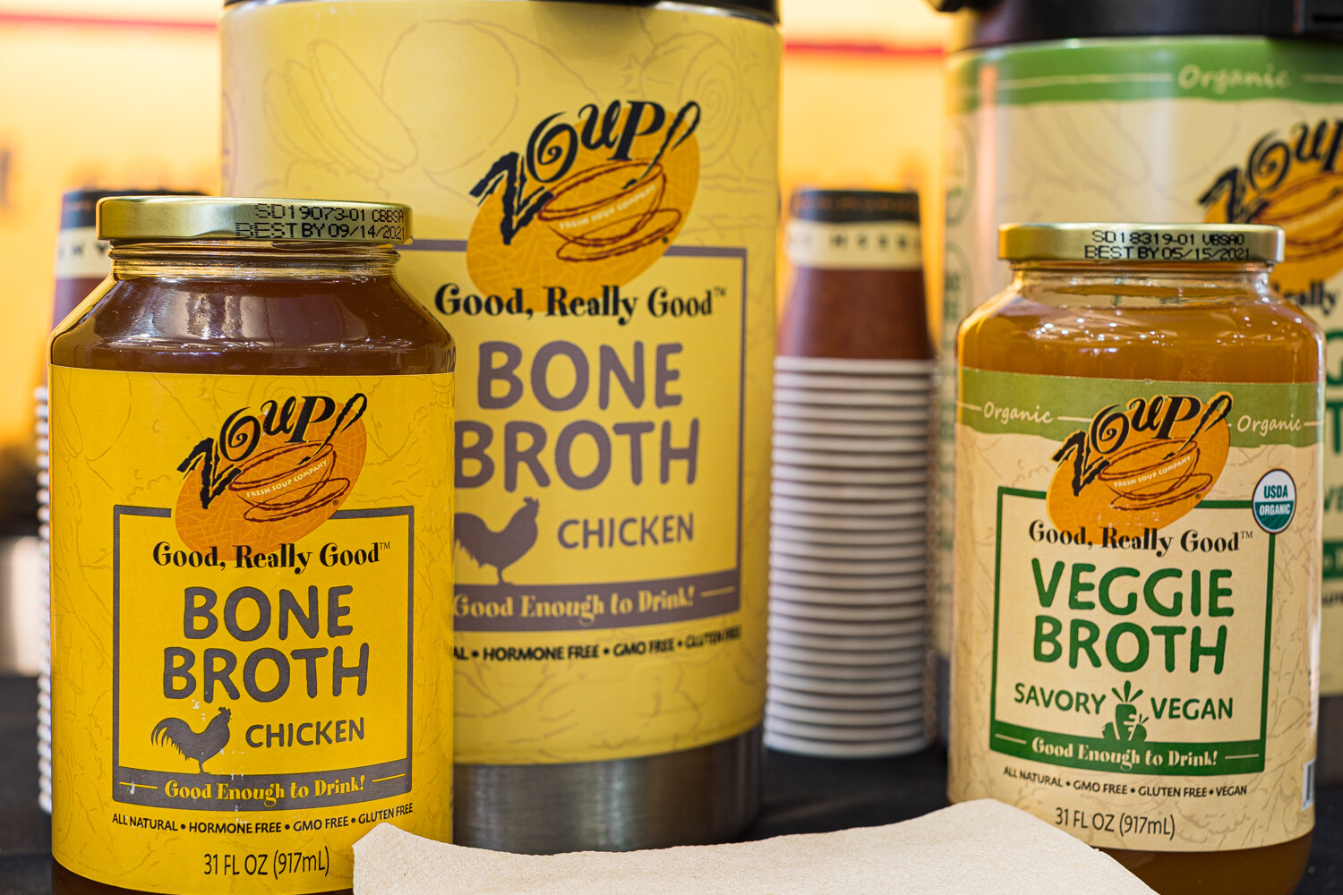 Large jars of Zoup! Bone Broth Chicken and Veggie Broth with yellow and green labels.